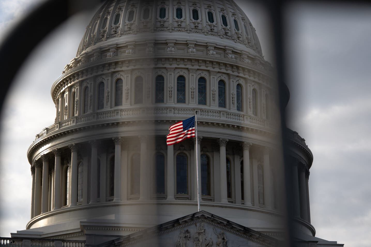 El Capitolio de Estados Unidos con la bandera estadounidense ondeando frente a su cúpula, visto a través de una reja, en Washington D.C.