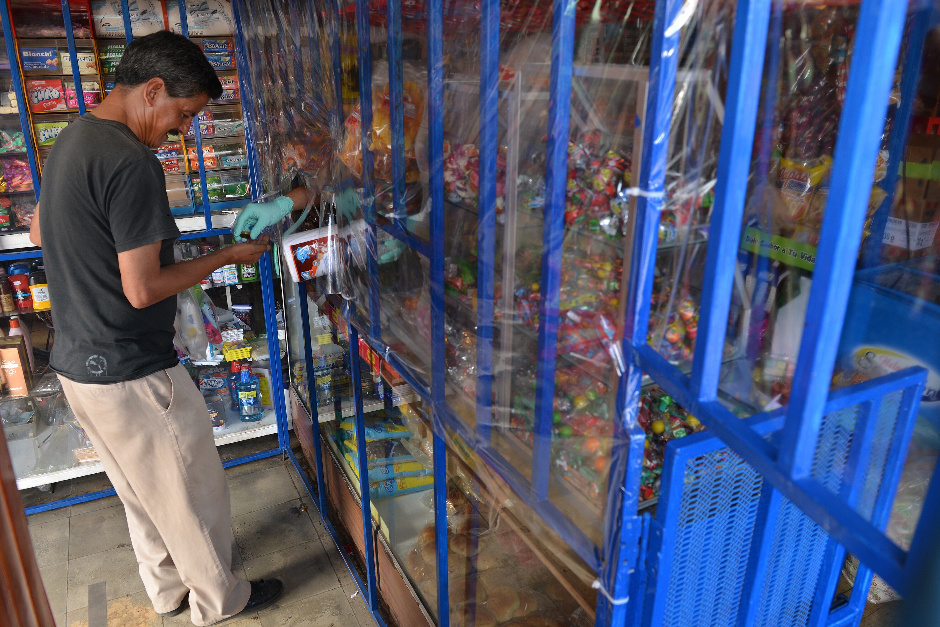 Hombre atendiendo un cliente en un negocio en Costa Rica, con vitrinas llenas de productos y una barrera de plástico transparente.