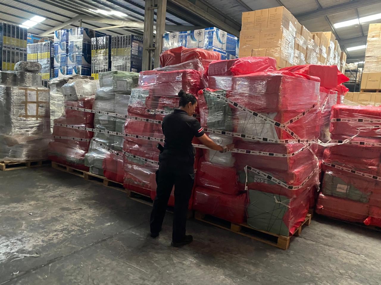 Oficial de la Policía de Control Fiscal inspecciona pallets con mercancía embalada en un almacén, durante operativos de fiscalización a negocios tipo outlet en coordinación con Tributación y Aduanas en Costa Rica.