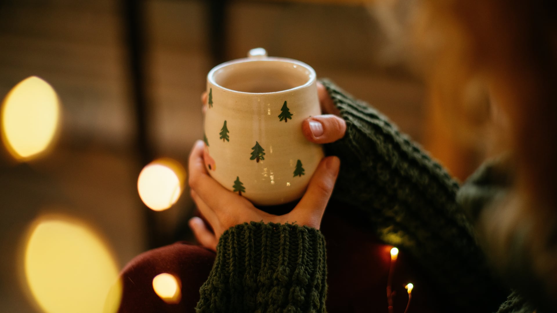 Tiempo de Navidad, época navideña, manos sosteniendo una taza con dibujo de árboles de Navidad