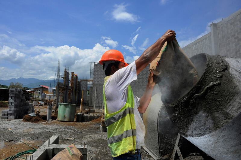 Obrero con casco y chaleco de seguridad vaciando cemento en una mezcladora en una obra en Costa Rica. La construcción de viviendas presenta costos diferenciados según el cantón.