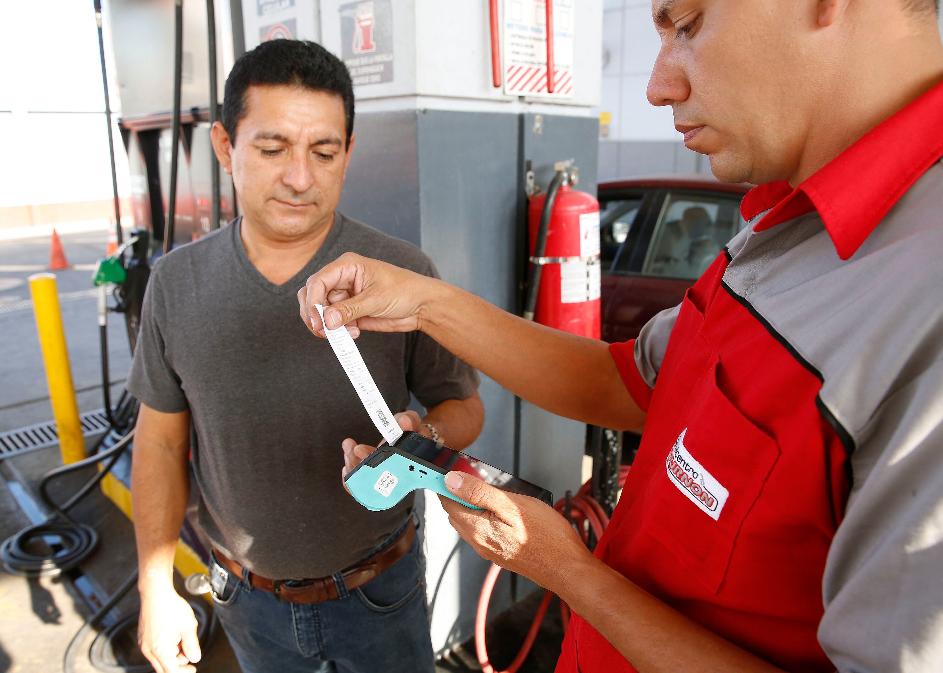 Un trabajador de estación de servicio entrega un comprobante electrónico a un cliente tras una compra de combustible, como parte del sistema de facturación digital en Costa Rica.