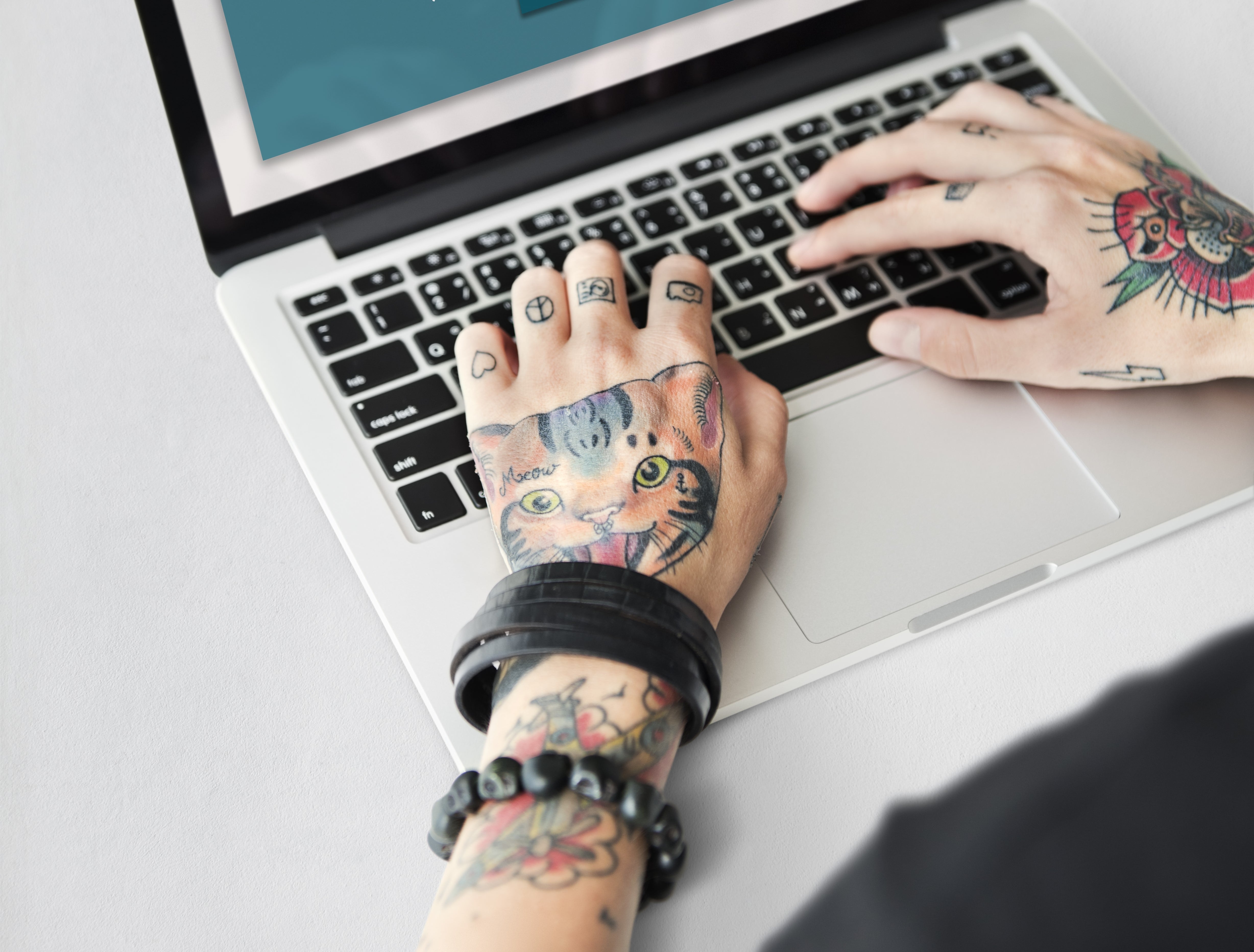 Manos de joven con tatuajes y pulseras, sobre teclado de laptop