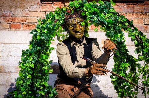 Artista callejero disfrazado de guardián de la naturaleza con hojas verdes y vestimenta rústica en un entorno urbano.