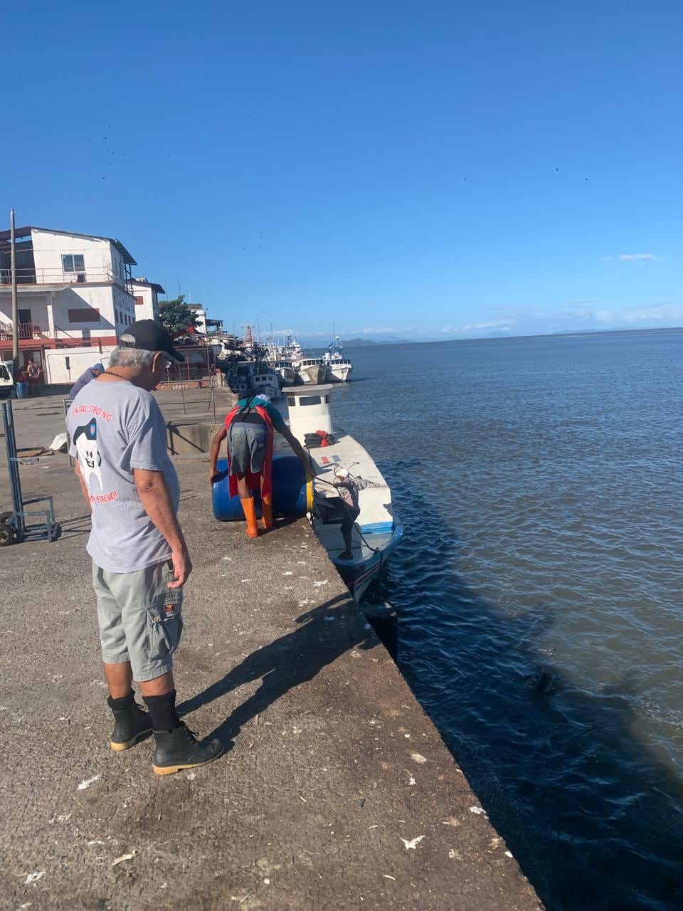 Un hombre bota las aguas residuales del Mercado de Puntarenas en el estero, otro lo observa.
