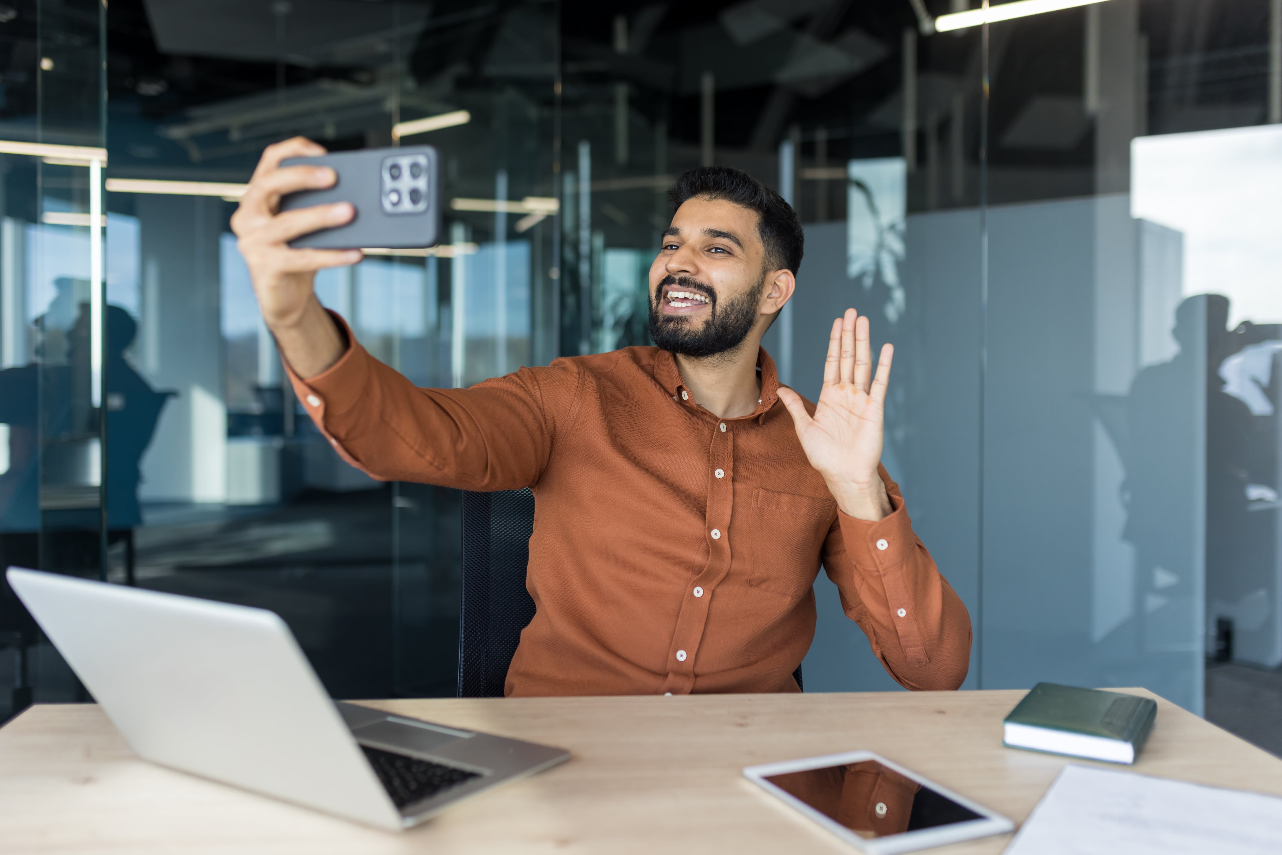 Hombre filmándose, haciéndose un video selfi en su escritorio, con su teléfono celular