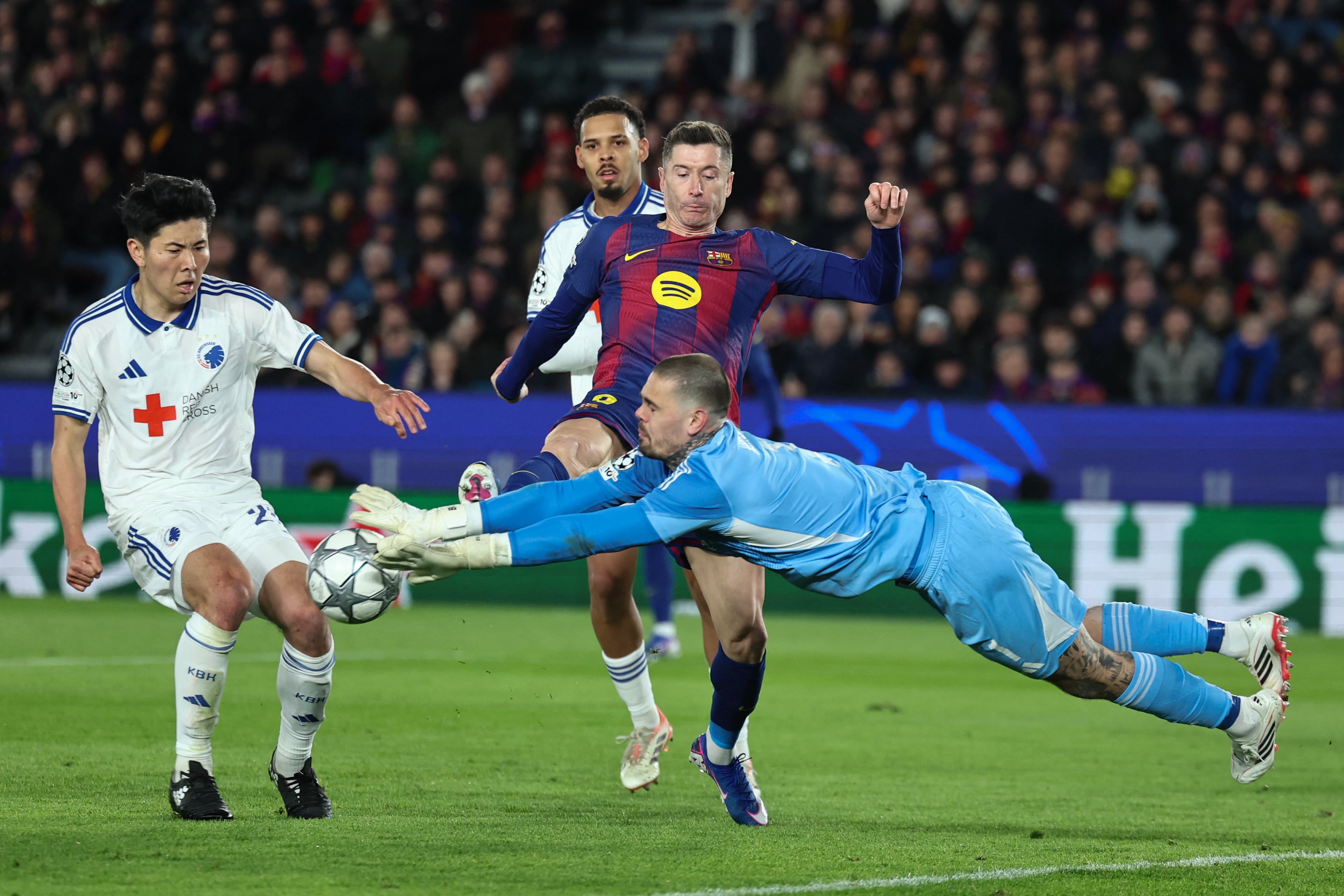 El arquero del Copenhage Dominik Kotarski se lanza en medio de la acción que protagonizan su compañero Junnosuke Suzuki y Robert Lewandowski del Barcelona, por la Champions League.