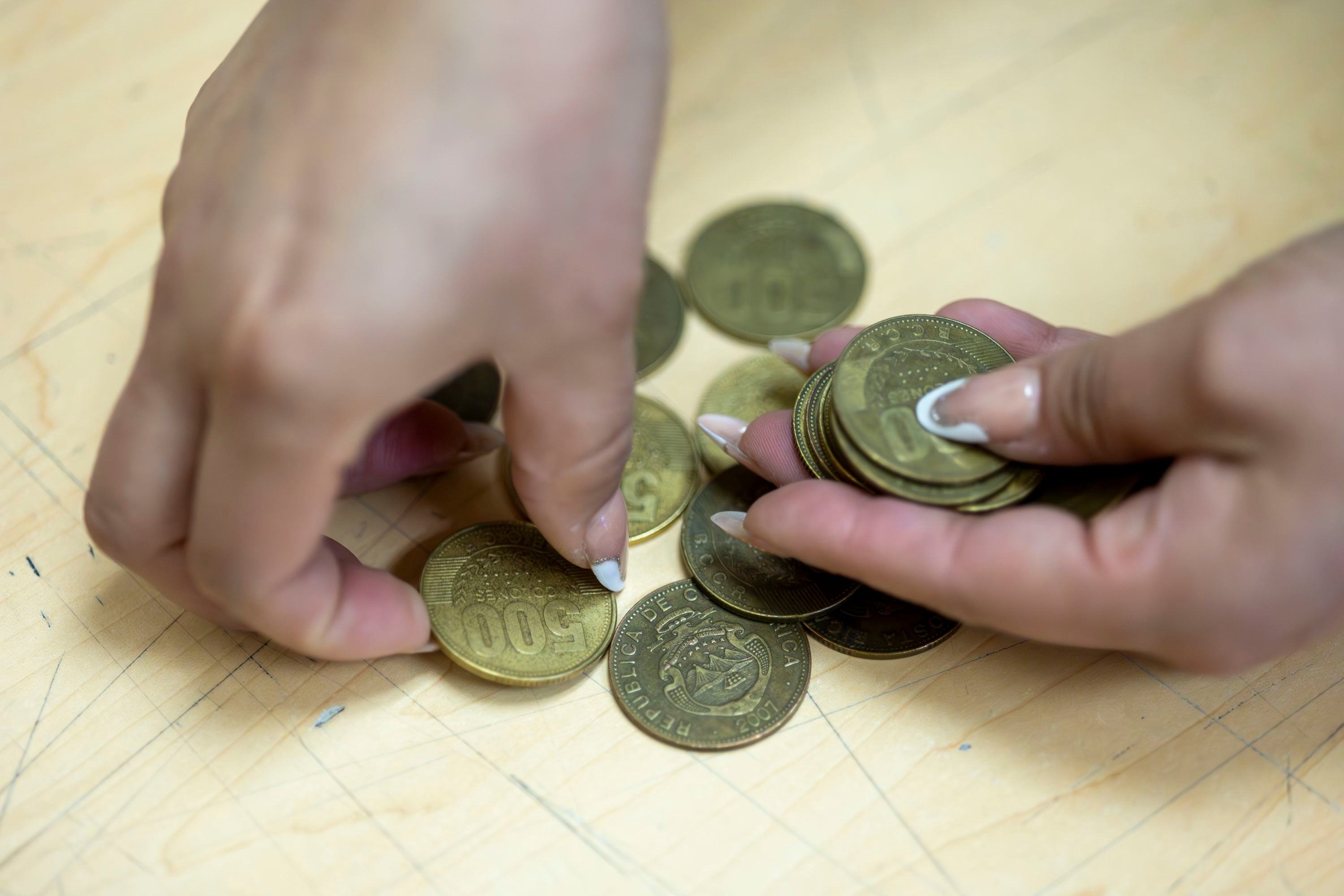 Manos de mujer cuentan un grupo de monedas de ¢500.