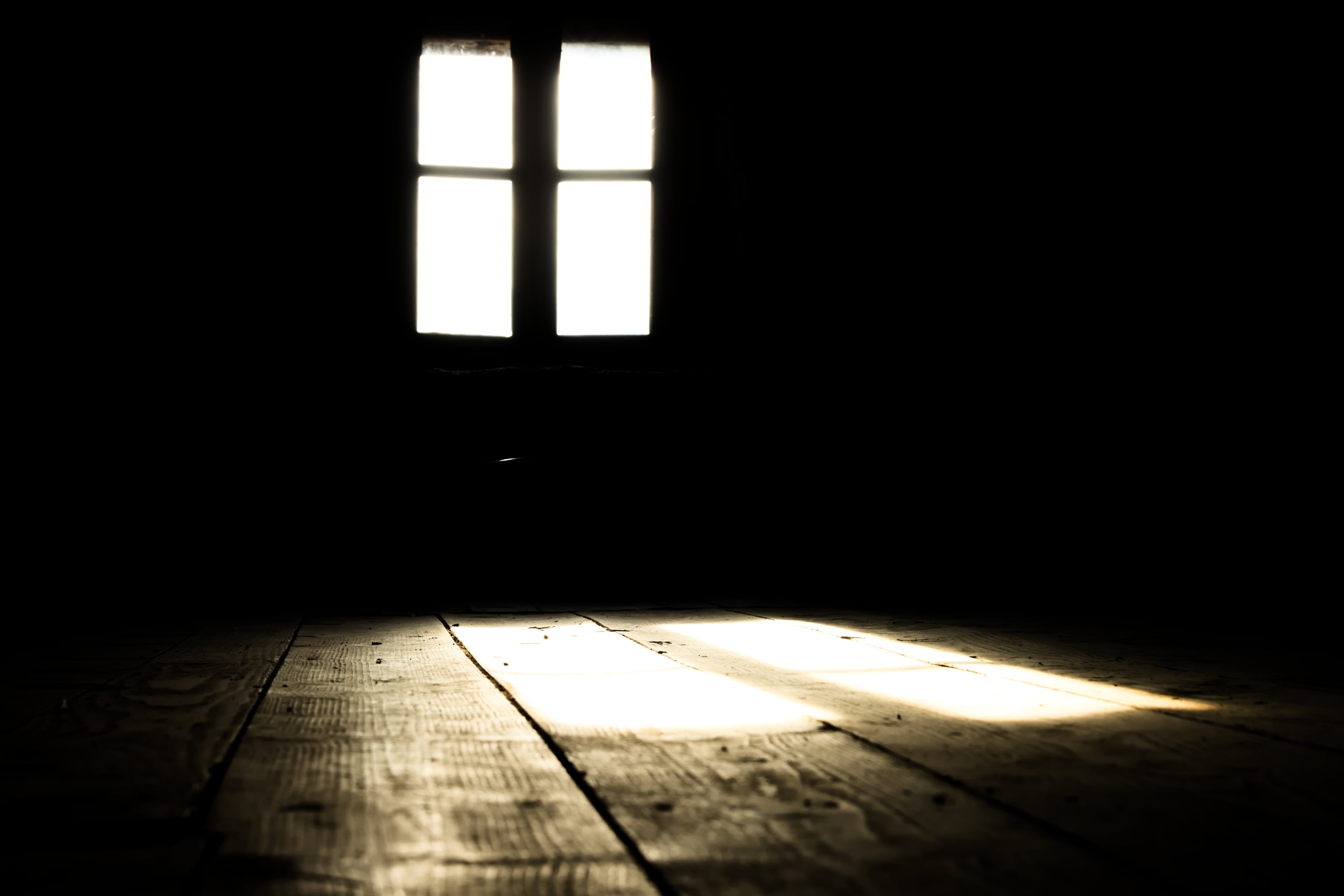 Luz se cuela por una ventana e ilumina una habitación oscura y abandonada, con piso de tablones de madera
