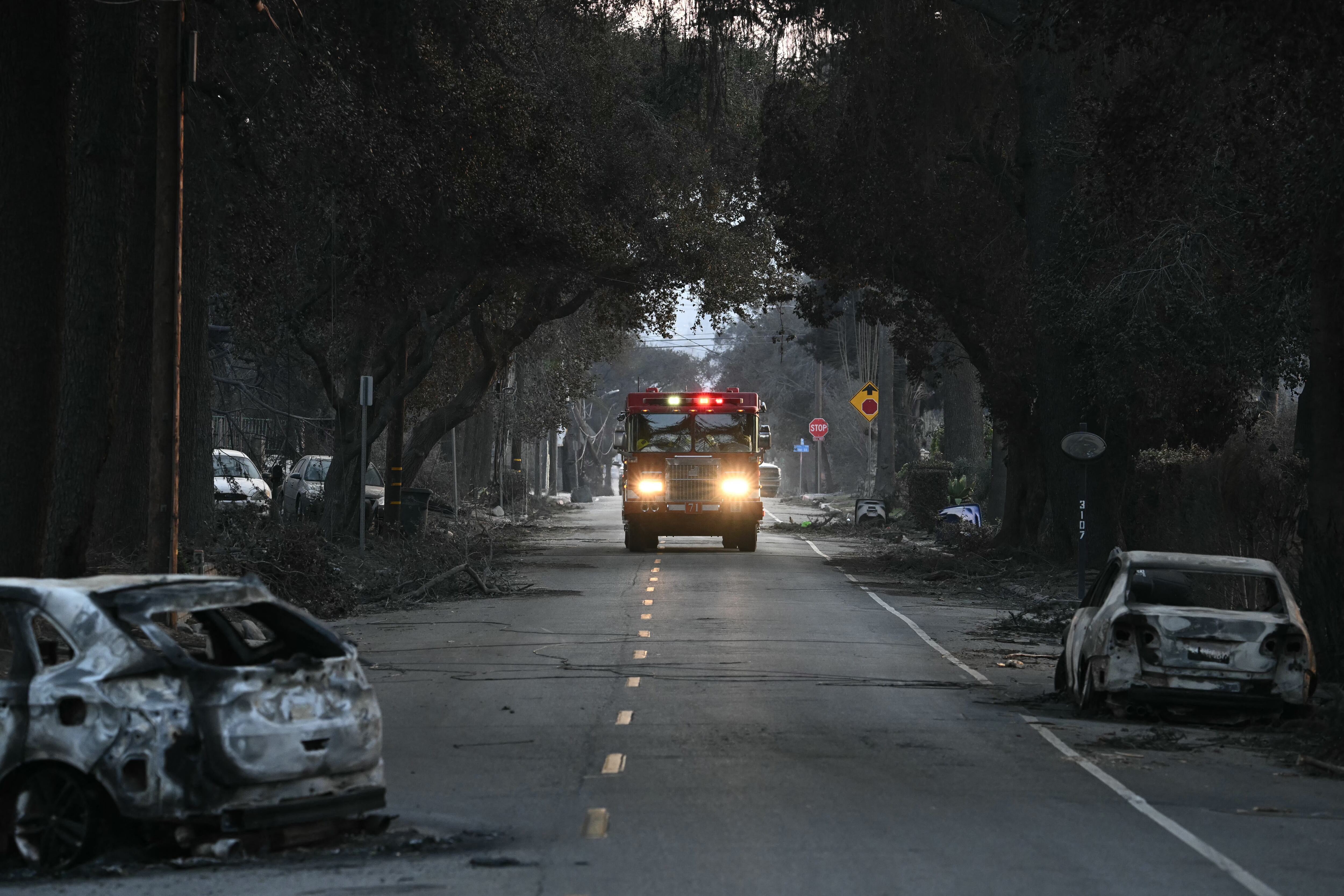 Un camión de bomberos avanza por una calle con vehículos calcinados por el incendio de Eaton en Altadena, California.