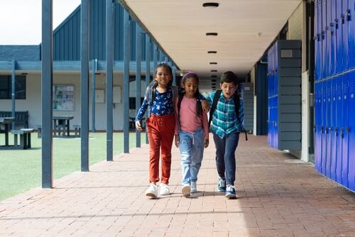 Niños estudiantes caminan abrazados en la escula para ilustrar el aprendizaje de la convivencia pacífica desde temprana edad.