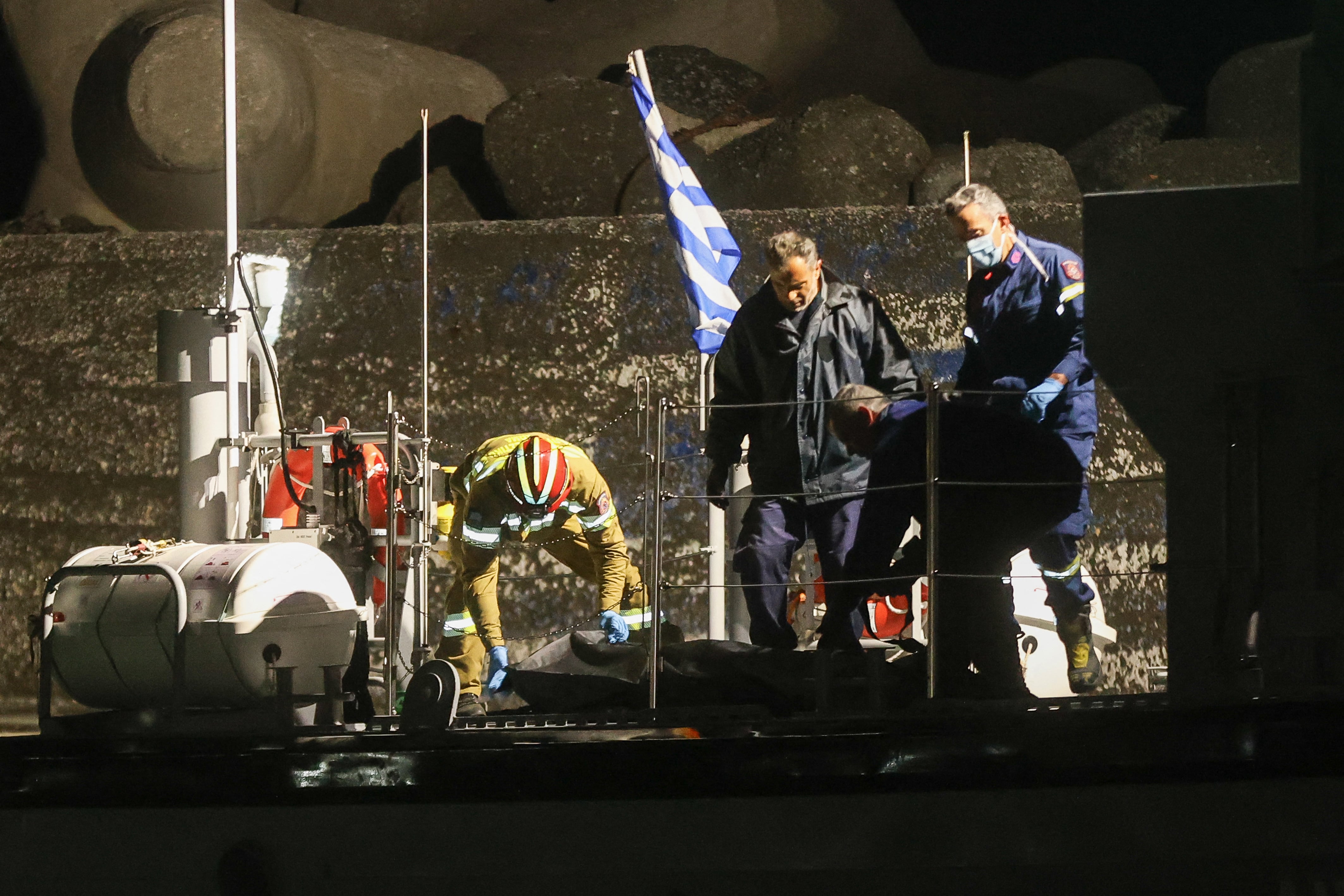 Bomberos y miembros de la guardia costera helénica transportan bolsas con cuerpos desde una embarcación de la guardia costera después de que un buque de migrantes se hundiera frente a la costa, en el puerto de Ierapetra, en la isla de Creta, este sábado.