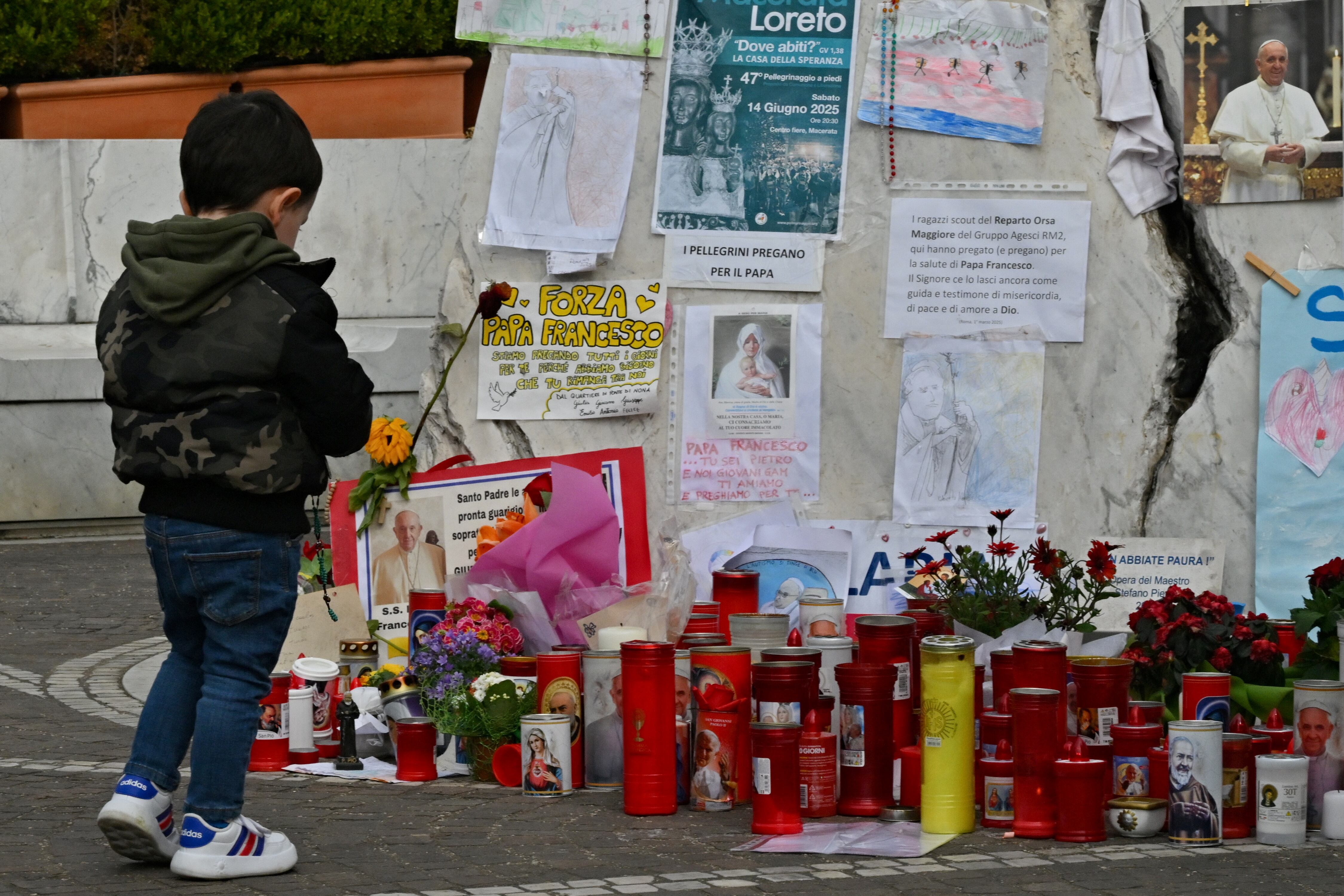 Un niño posa junto a la estatua de Juan Pablo II, en el exterior del Hospital Universitario Gemelli, donde el papa Francisco está internado por neumonía. Foto: