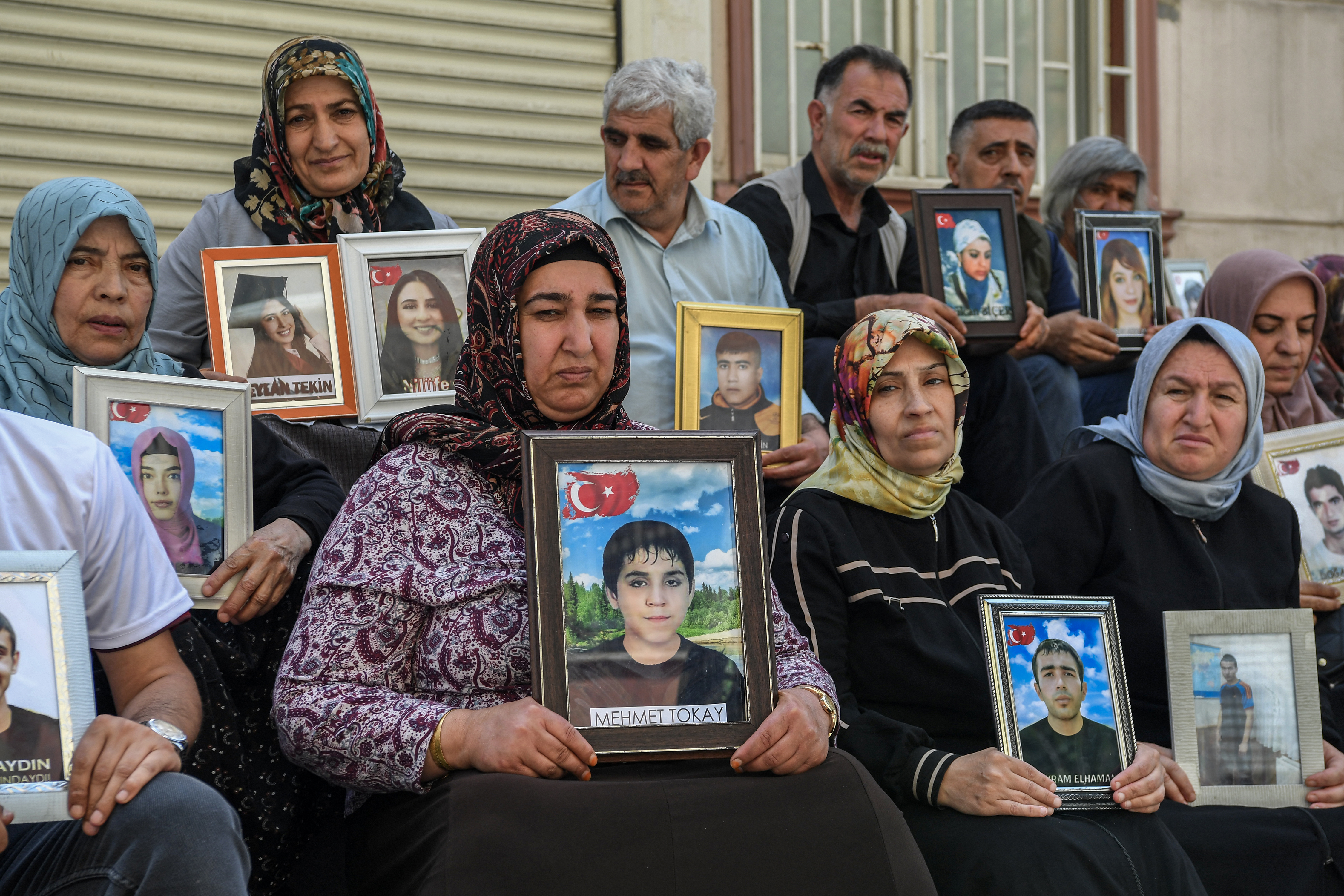 Familias cuyos hijos se unieron al PKK (Partido de los Trabajadores del Kurdistán) sostienen sus imágenes sentadas frente a la sede del Partido Igualdad y Democracia (DEM) tras el anuncio del PKK de su disolución, en la ciudad de Diyarbakir, de mayoría kurda, al oeste de Turquía, este 12 de mayo. Fotografía: