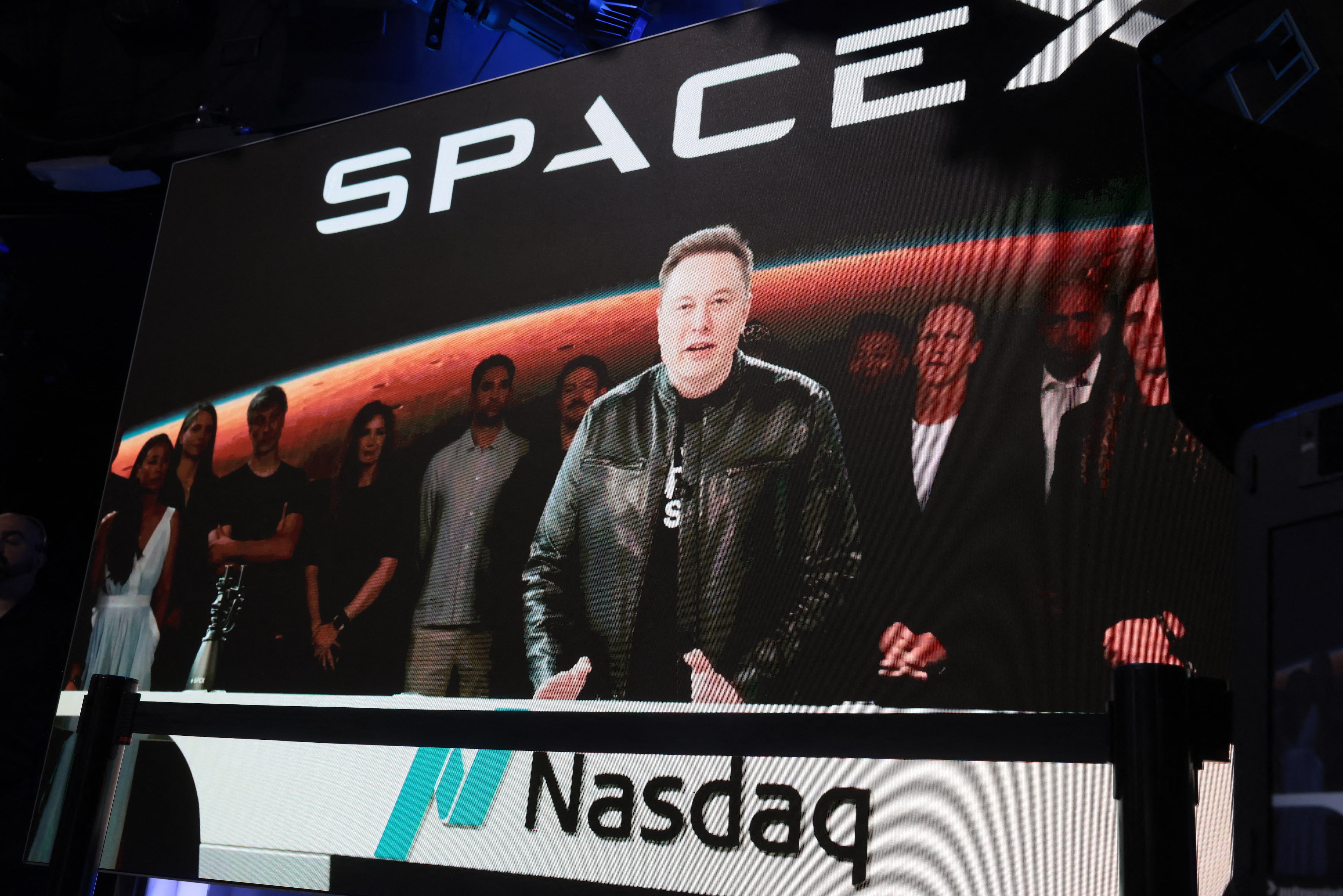 Una pantalla gigante muestra a Elon Musk durante la ceremonia de salida a bolsa de SpaceX en el Nasdaq. La imagen exhibe el logotipo de la compañía aeroespacial y el símbolo del mercado tecnológico estadounidense.