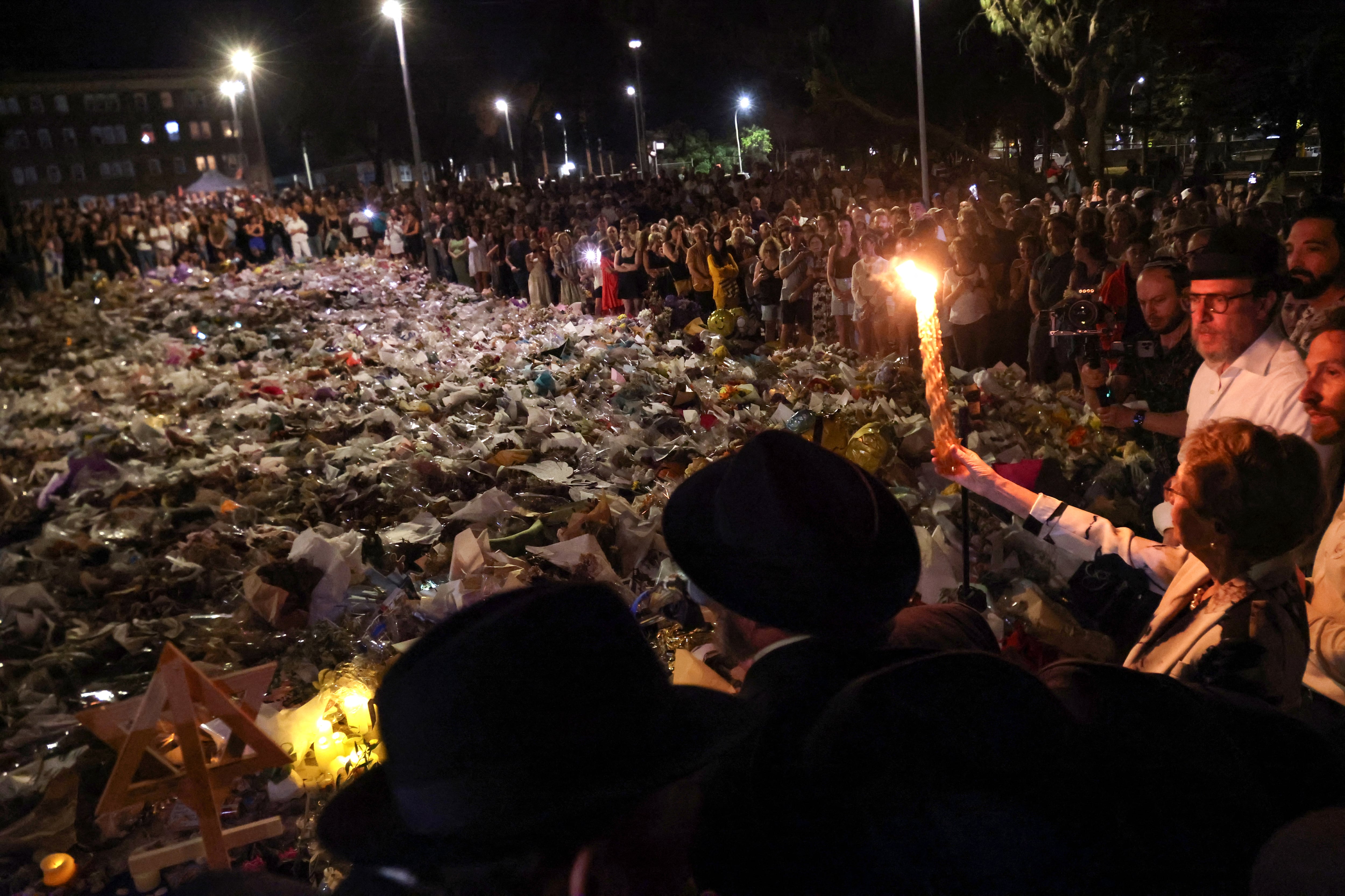 Se alza una vela antes del séptimo encendido de la festividad judía de Janucá, mientras los dolientes se colocan junto a ofrendas florales en memoria de las víctimas del tiroteo en Bondi Beach, Sídney, el 20 de diciembre de 2025. Padre e hijo armados están acusados de disparar contra la multitud en una festividad judía en la playa el 14 de diciembre, matando a 15 personas en un ataque que las autoridades vincularon con la ideología del Estado Islámico.