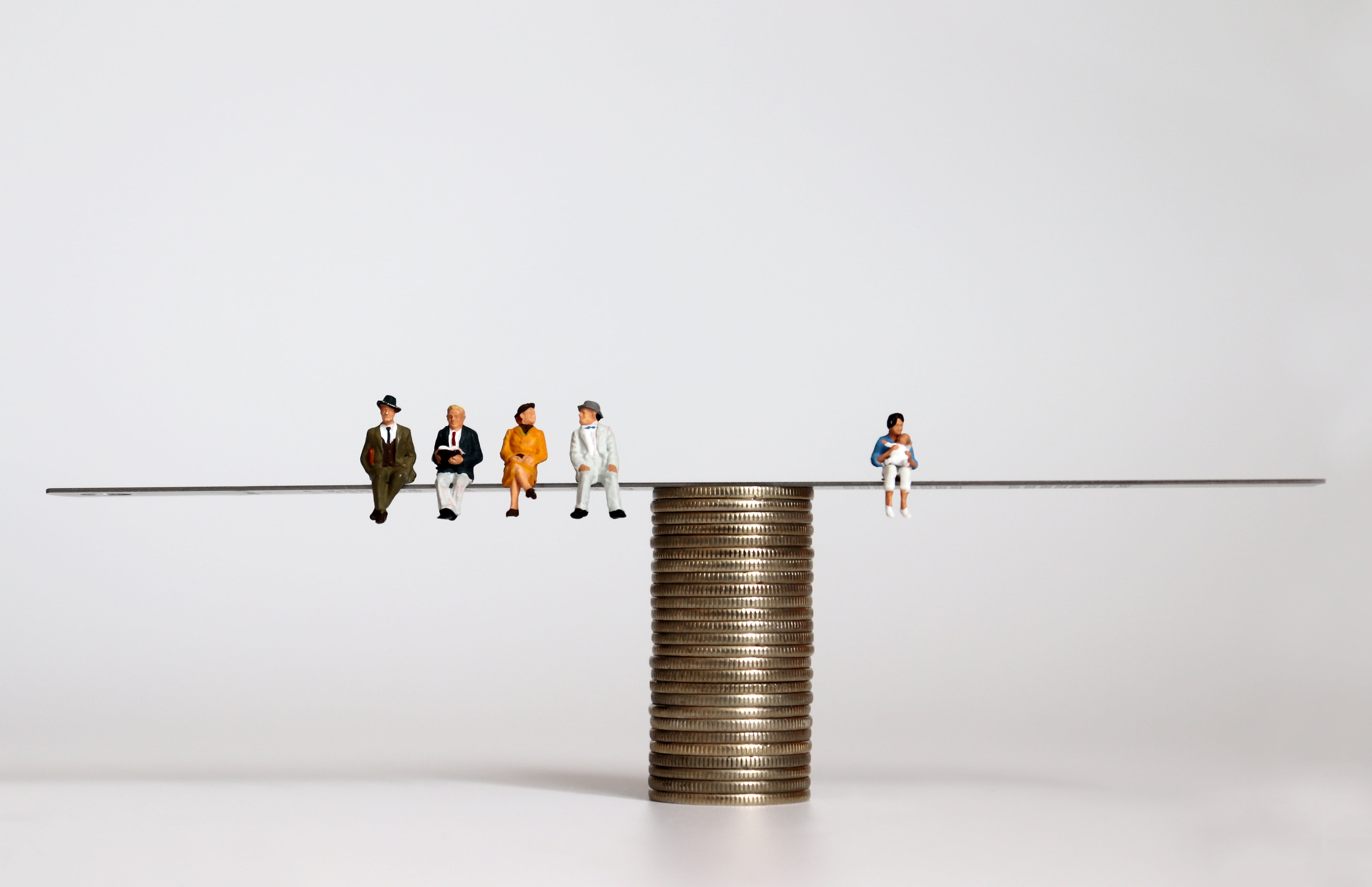 Muñecos sentados en una frágil tabla sobre una pila de monedas