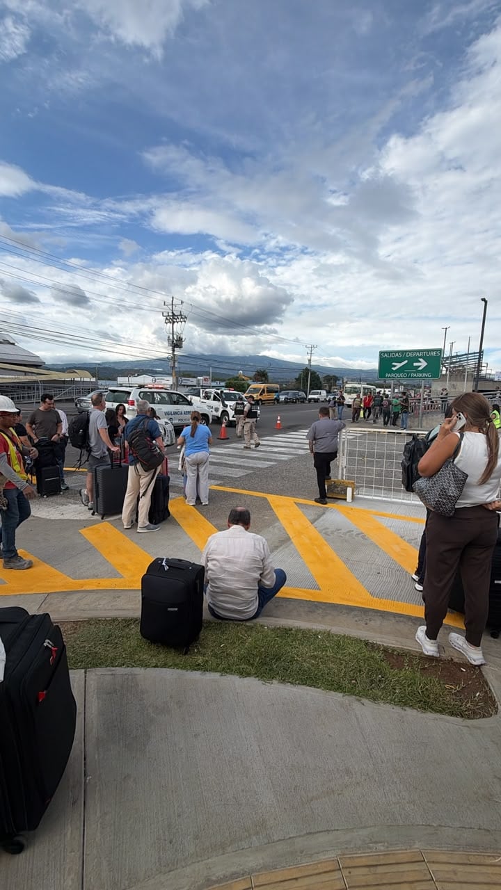 Los pasajeros con vuelos internacionales permanecen en las afueras del aeropuerto internacional Juan Santamaría, mientras las autoridades investigan una alerta de un vehículo con armas y drogas en la zona.