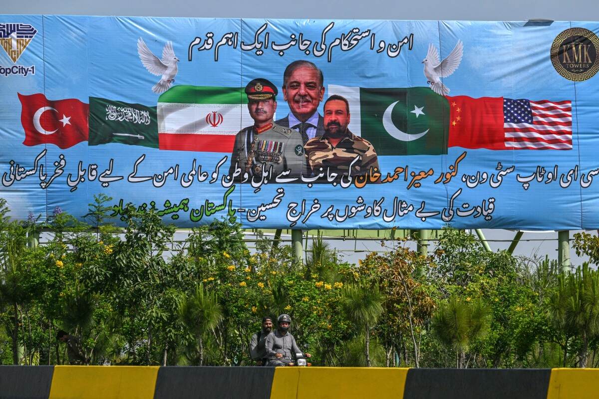 Motociclistas pasan junto a un cartel publicitario con el primer ministro de Pakistán, Shehbaz Sharif (centro), y el jefe del Ejército y mariscal de campo Syed Asim Munir (izq.), en Islamabad el 20 de abril de 2026, antes de las previstas conversaciones de paz entre Estados Unidos e Irán.