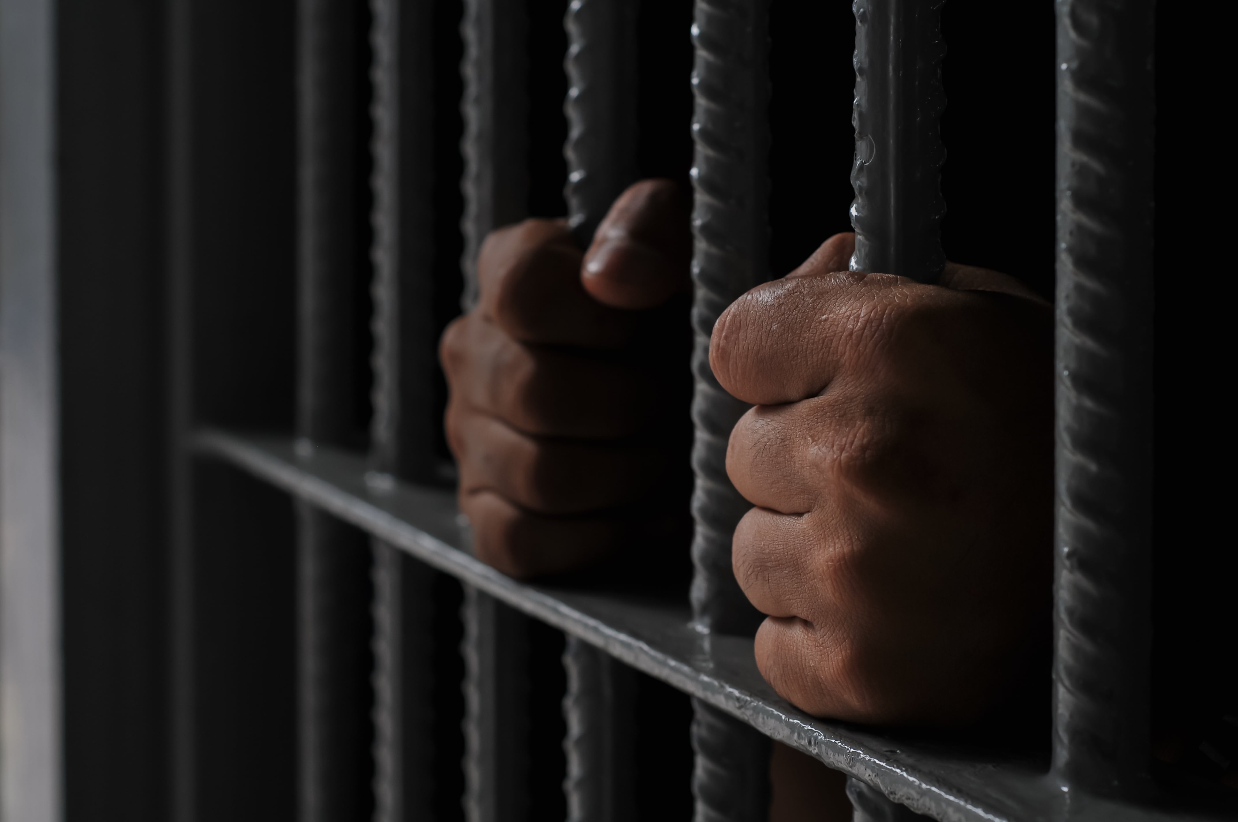 Cárcel, prisión, encarcelamiento. Detalle de manos sujetando barrotes en celda de un penal