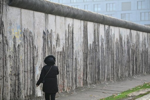 Mujer camina junto a segmentos del Muro de Berlín durante el 35.º aniversario de su caída, en noviembre de 2024, marcando el fin del comunismo y la reunificación alemana.
