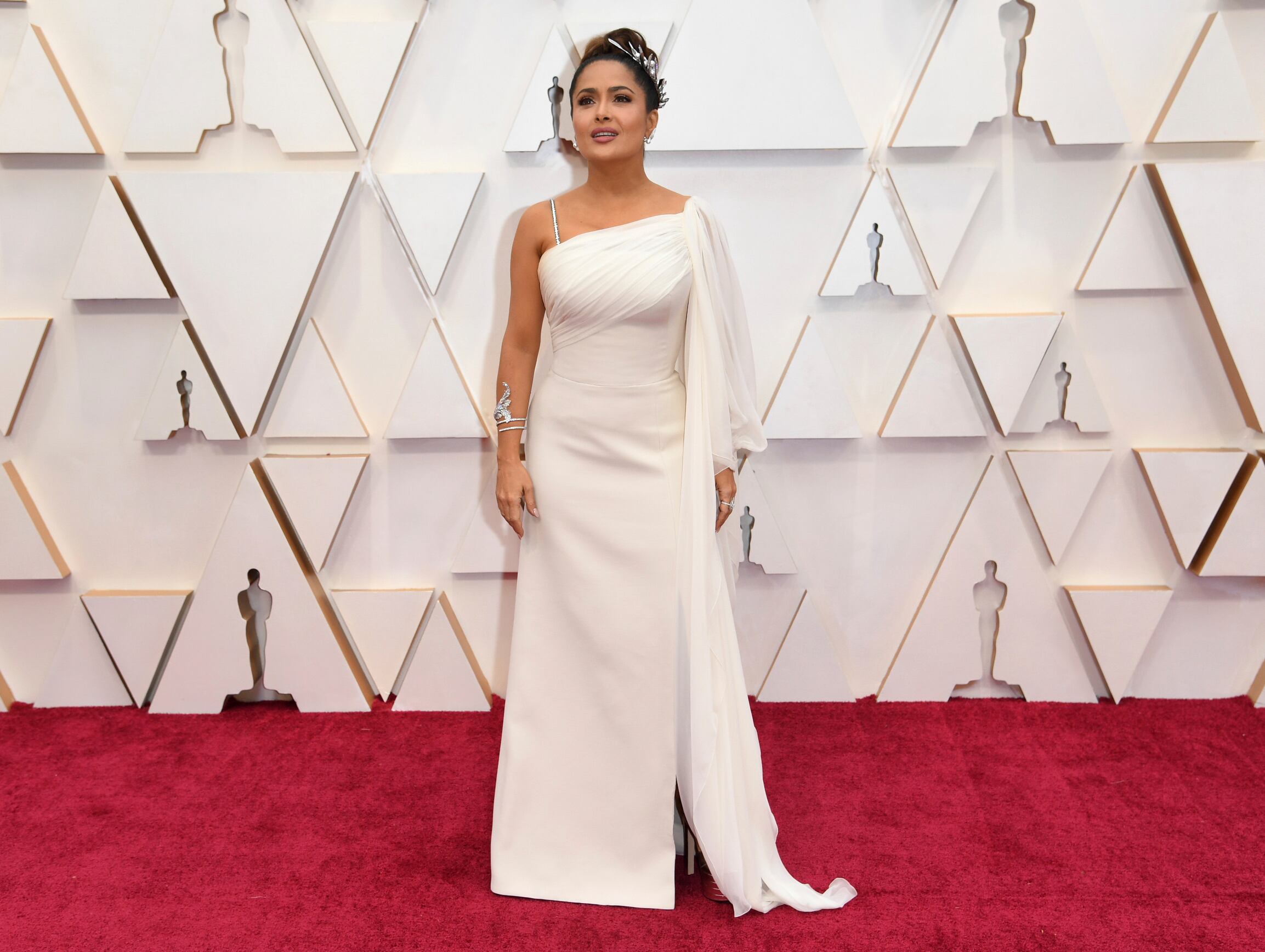Salma Hayek en una alfombra roja de los premios Óscar. Usa un vestido blanco largo y el cabello recogido.