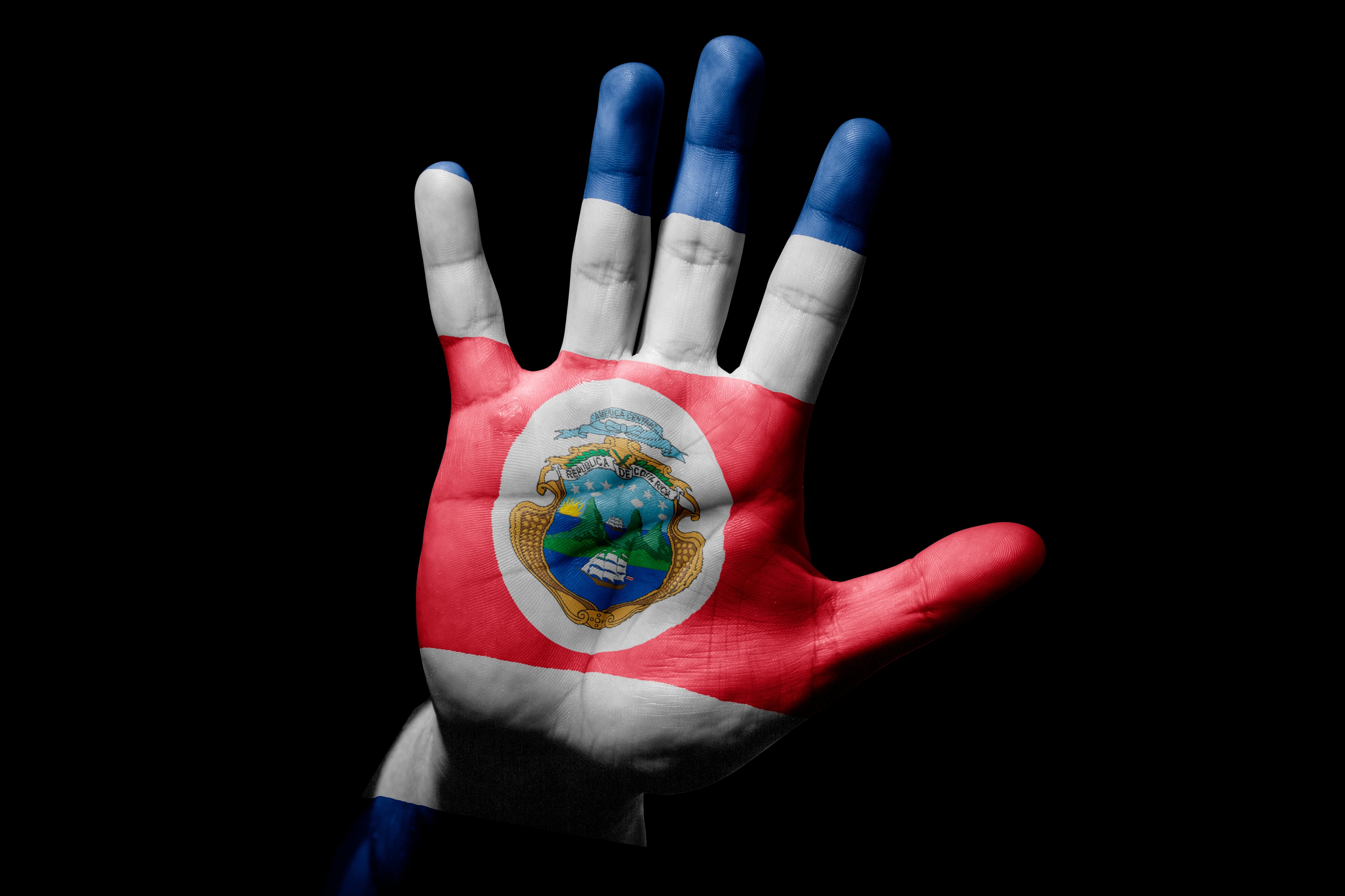 Palma de mano pintada con los colores de la bandera de Costa Rica y haciendo la señal de alto, basta, no más, pausa