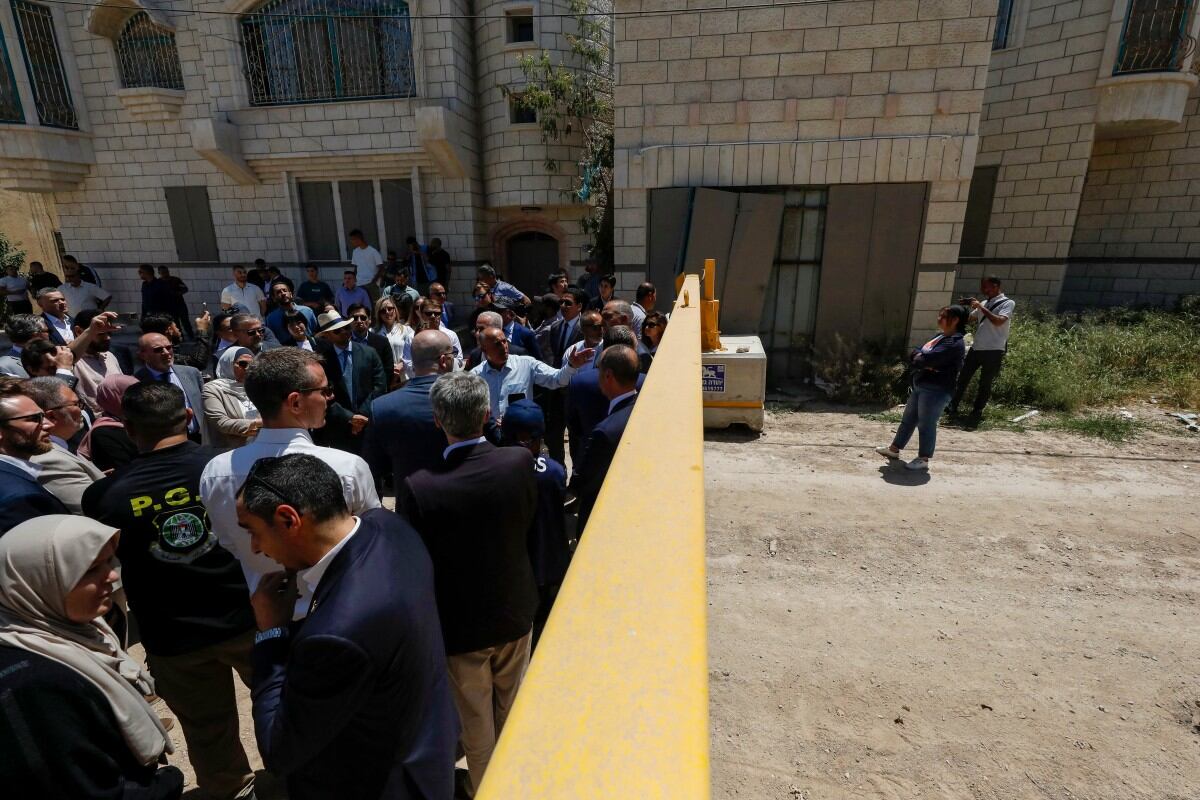 Miembros de una delegación diplomática de la Unión Europea permanecen detrás de una reja en la entrada este del campo de refugiados de Yenín durante una visita a la ciudad de Yenín, el 21 de mayo de 2025, en medio de una ofensiva militar israelí en curso en la Cisjordania ocupada. La Autoridad Palestina acusó a las fuerzas israelíes de disparar contra diplomáticos mientras visitaban la conflictiva ciudad cisjordana de Yenín ese mismo día, y difundió un video en el que se ve a dos soldados apuntando con rifles a un grupo de personas. (Foto de Mohammad MANSOUR / AFP)