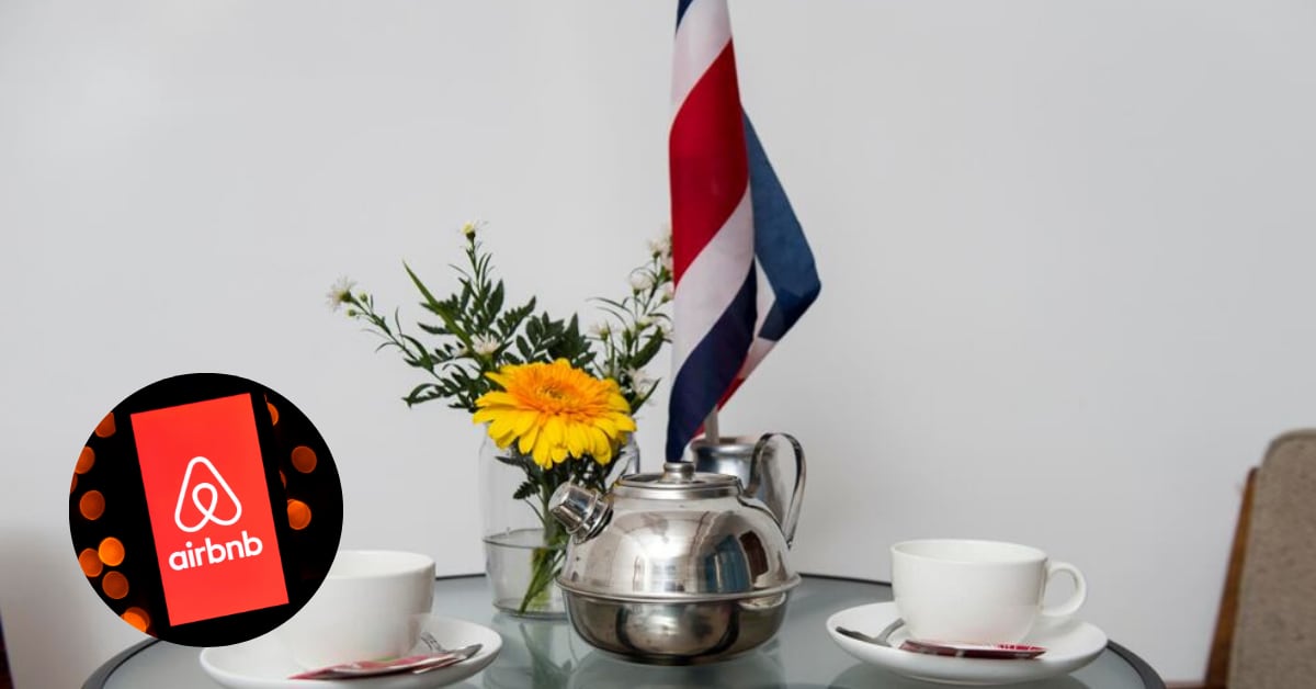 Logotipo de Airbnb en un teléfono móvil junto a una mesa con servicio de café y bandera de Costa Rica, en referencia a los 15 años de operación de la plataforma de hospedaje de corta estancia en el país y su impacto en el turismo interno.