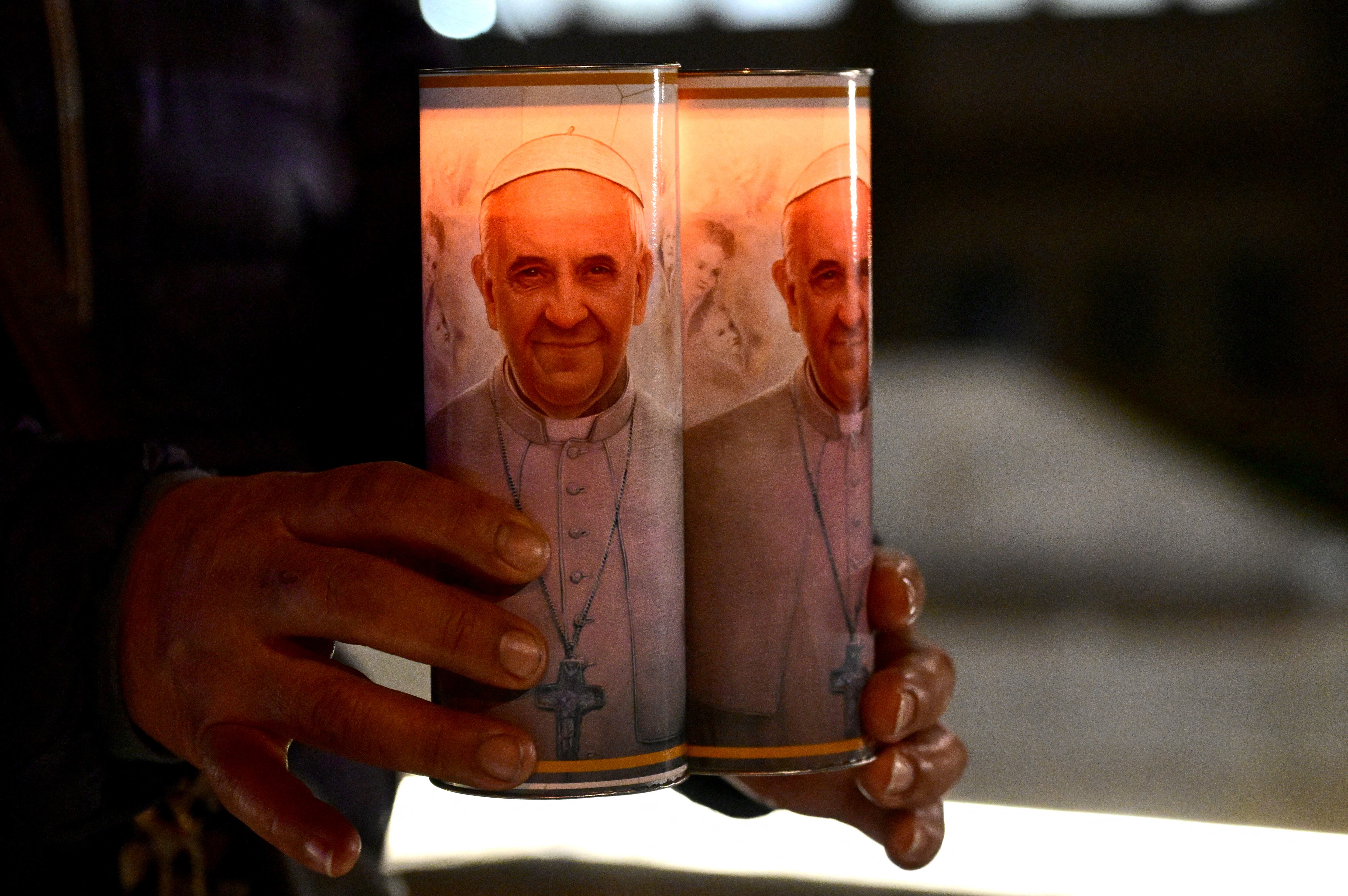 A faithful from Bolivia holds candles of Pope Francis near a statue of Pope John Paul II outside the Gemelli hospital where Pope Francis is hospitalized for tests and treatment for bronchitis in Rome, on February 18, 2025. (Photo by Tiziana FABI / AFP)
