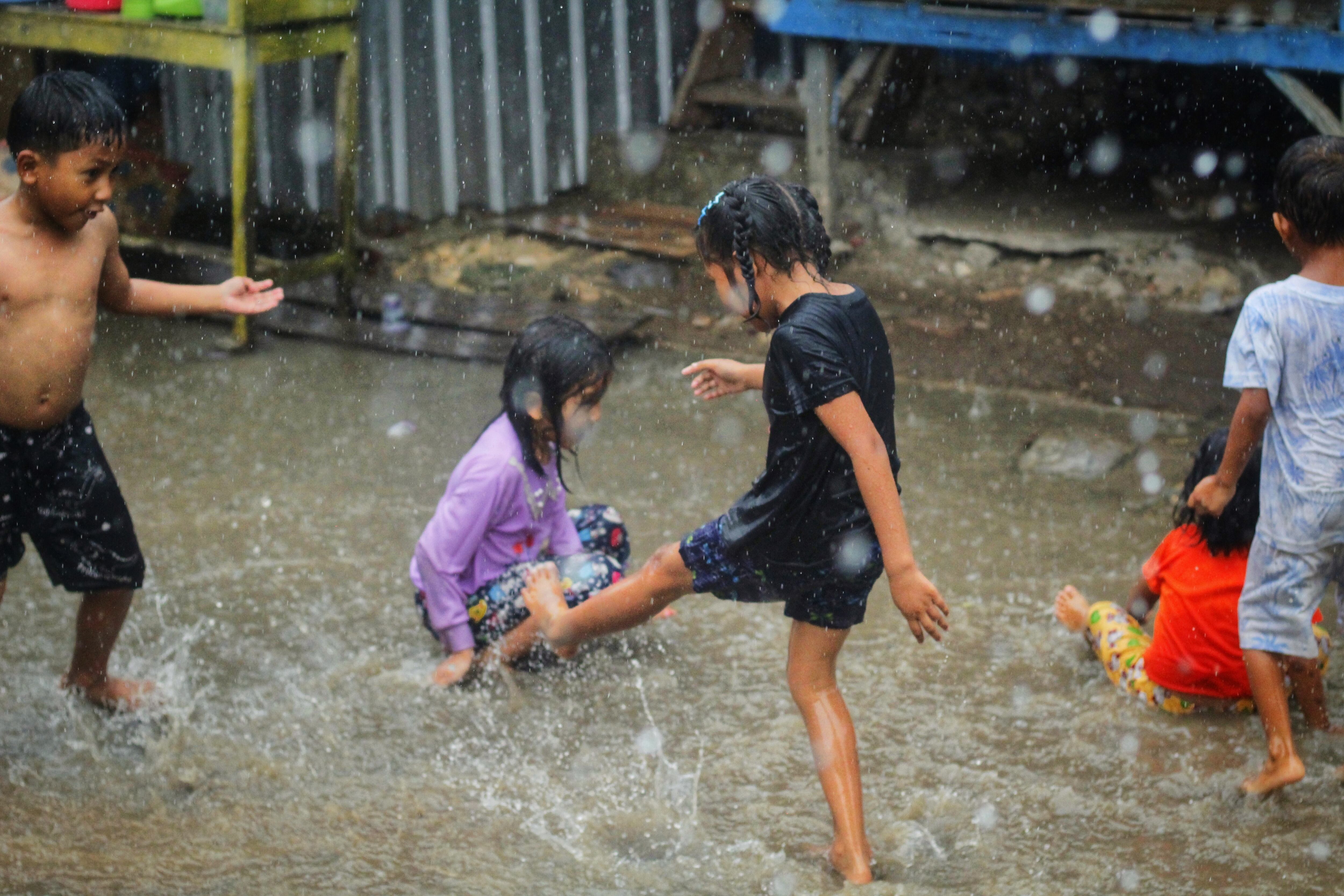 Niños descalzos jugando bajo la lluvia y en charcos