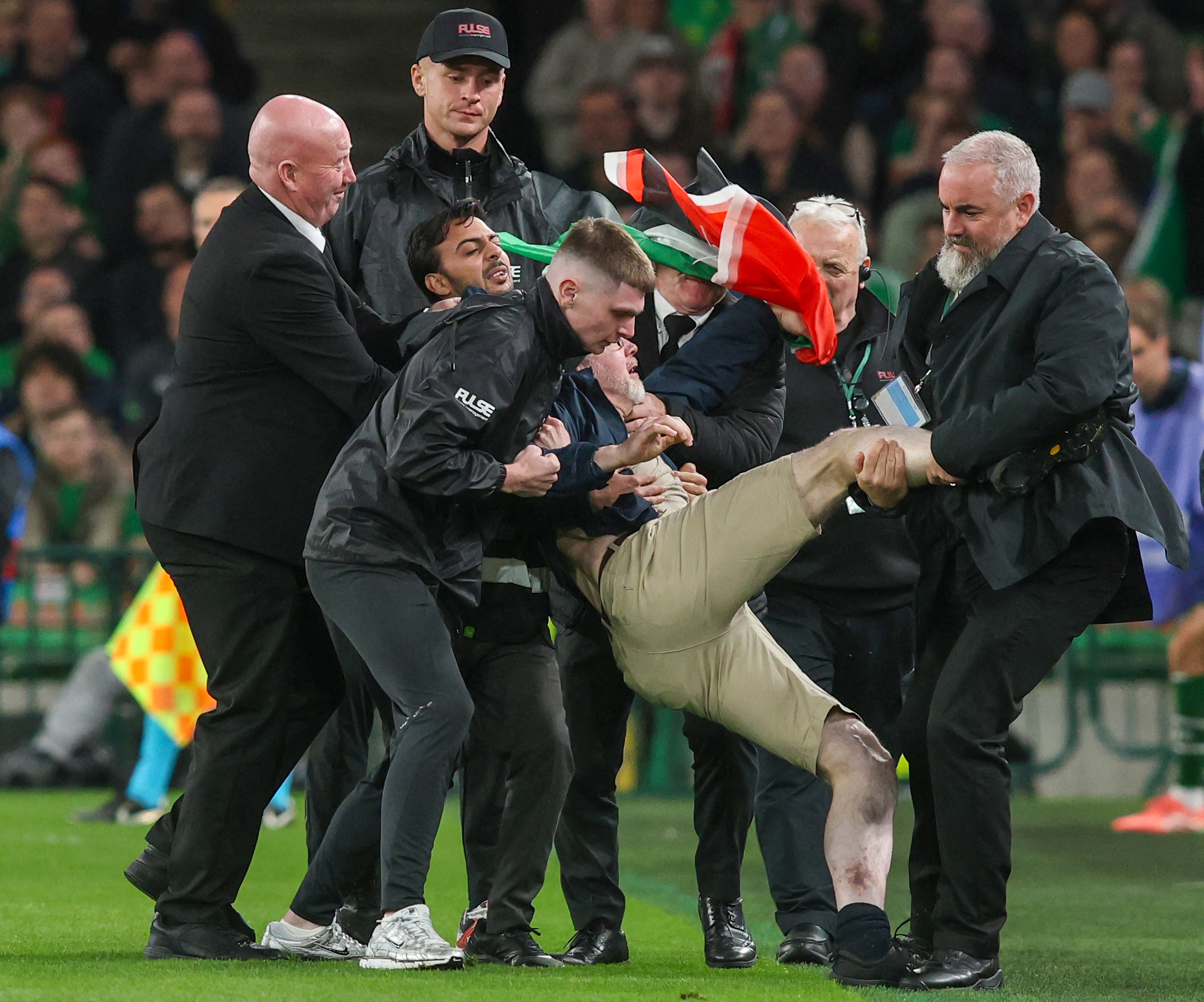 Agentes de seguridad retiran del campo a una persona que interrumpió con una bandera de Palestina el partido entre Irlanda y Austria, en Dublín, por la Nations League de Europa.
