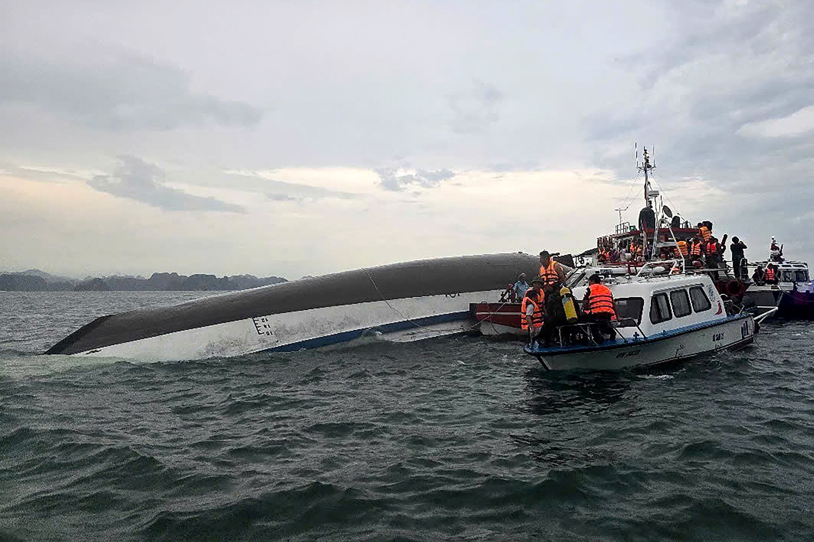 Esta fotografía distribuida, tomada el 19 de julio de 2025 y difundida por la Agencia de Noticias de Vietnam (VNA), muestra al personal de rescate reunido alrededor de un barco turístico volcado (izquierda) durante una operación de búsqueda y rescate en la bahía de Ha Long, provincia de Quang Ninh. Al menos 18 personas murieron y decenas permanecen desaparecidas luego de que un barco turístico con más de 50 personas a bordo volcara el 19 de julio en la bahía de Ha Long, según medios estatales. (Foto de Vietnam News Agency / AFP) / USO EDITORIAL ÚNICAMENTE – CRÉDITO OBLIGATORIO "AFP PHOTO / VIETNAM NEWS AGENCY (VNA)" – MATERIAL DISTRIBUIDO – PROHIBIDO USO PUBLICITARIO O COMERCIAL – DISTRIBUIDO COMO SERVICIO A CLIENTES.