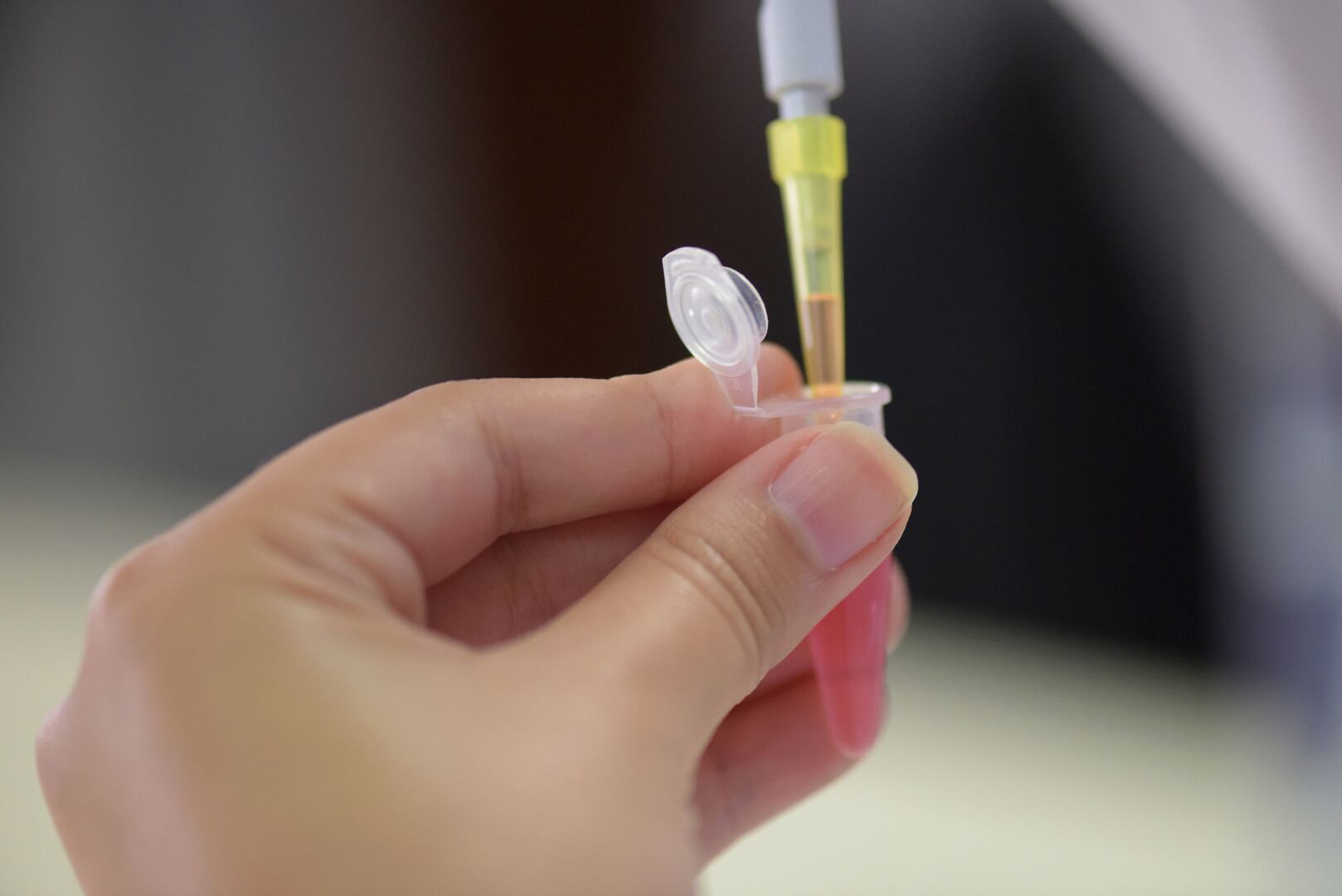 Una mano sostiene una pipeta de laboratorio y un pequeño tubo de ensayo.