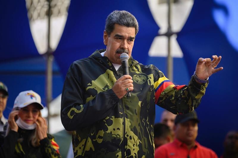 Nicolás Maduro habla durante un evento, vestido con chaqueta militar, mientras gesticula con una mano y sostiene un micrófono con la otra.