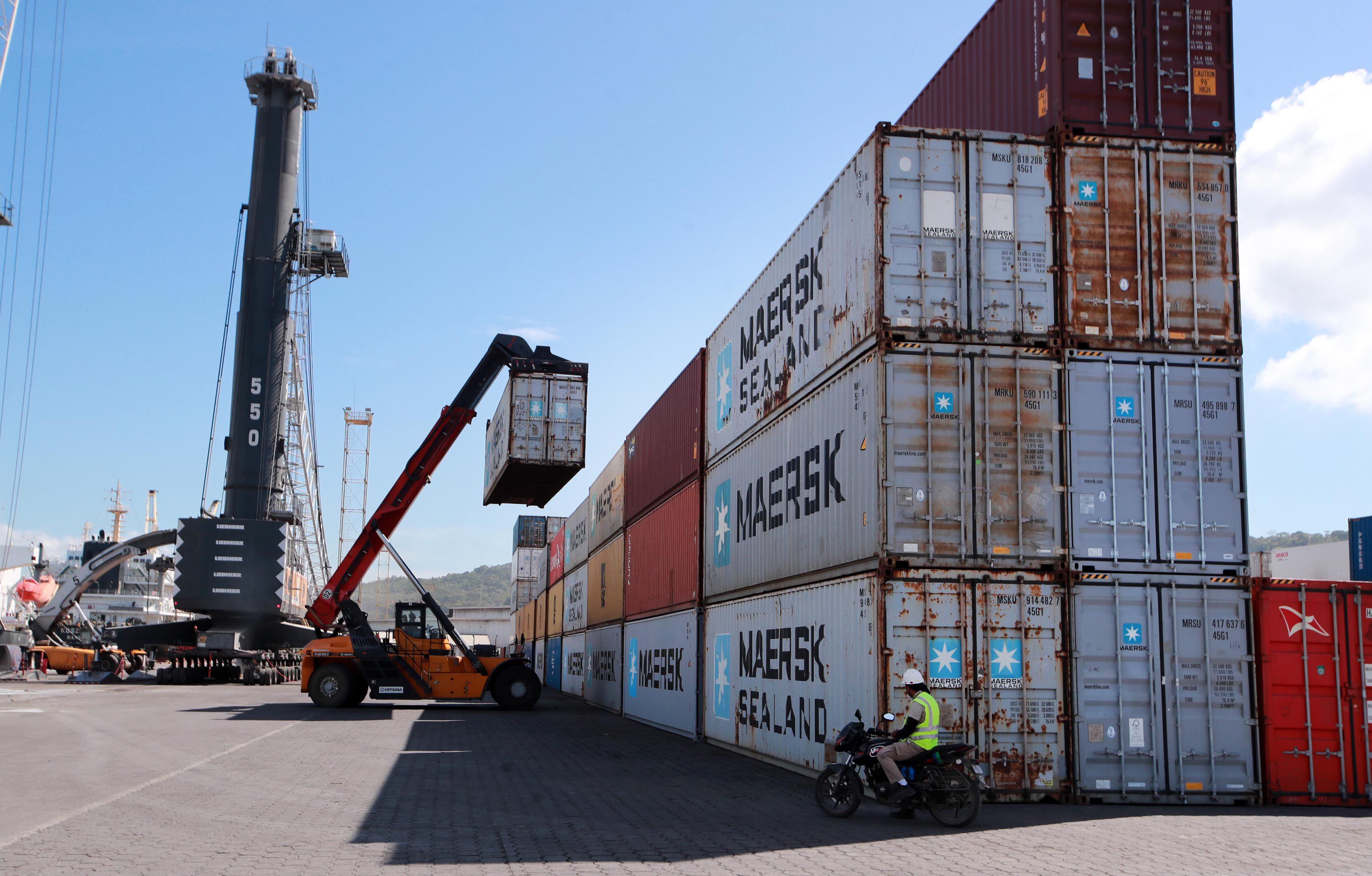 Operador con grúa movilizando contenedores en un puerto de Costa Rica bajo un cielo despejado, actividad relacionada con la exportación y comercio internacional.