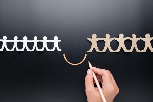 Una mano dibuja un puente que conecta dos grupos de figuras recortadas, simbolizando la unión y la reducción de divisiones.