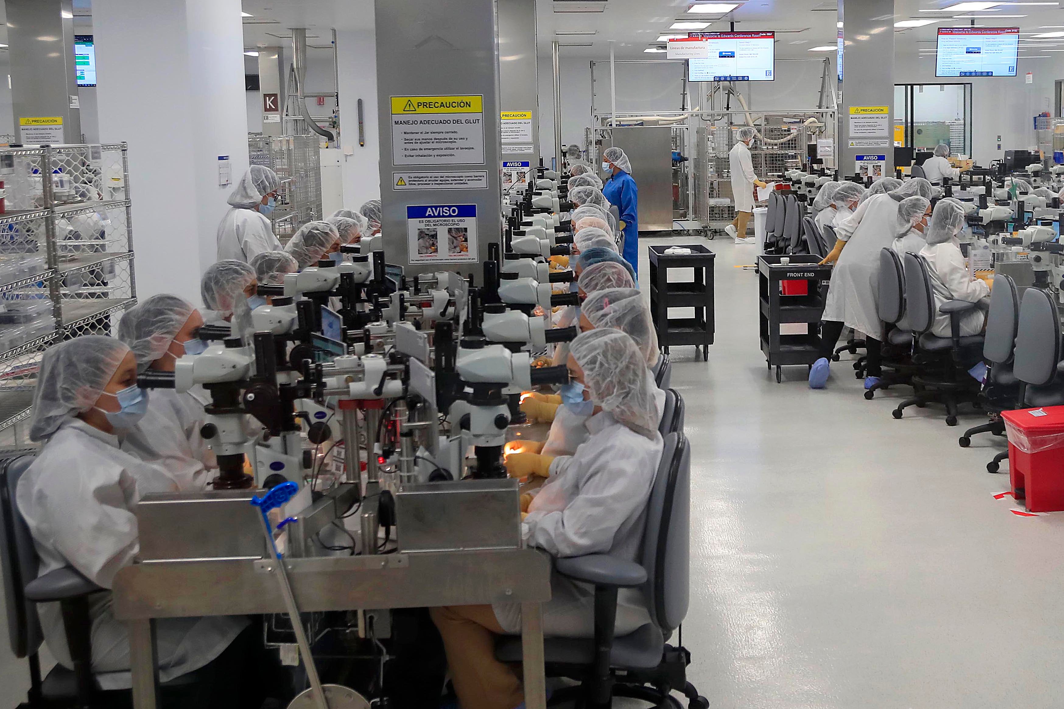 Operarios con batas y gorros de protección trabajan en una línea de producción de dispositivos médicos en una planta de manufactura en Costa Rica.