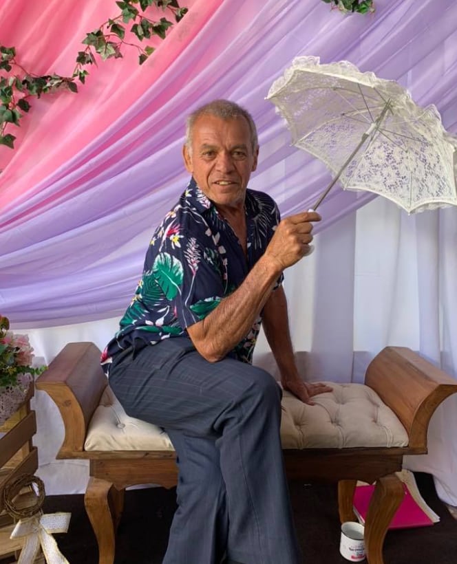 Imagen del cantante costarricense Roberto Quesada sentado en un sillón con la pierna cruzada y sosteniendo una sombrilla blanca.