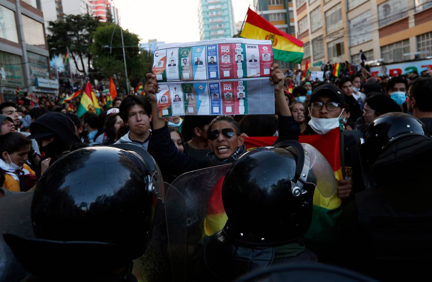 A youth hold ups an unmarked election ballot before police guarding the top election court where ballots are counted, as people protest partial presidential election results in La Paz, Bolivia, Tuesday, Oct. 22, 2019. International election monitors expressed concern over Bolivia's presidential election process Tuesday after an oddly delayed official quick count showed President Evo Morales near an outright first-round victory — even as a more formal tally tended to show him heading for a risky runoff. (AP Photo/Juan Karita)
