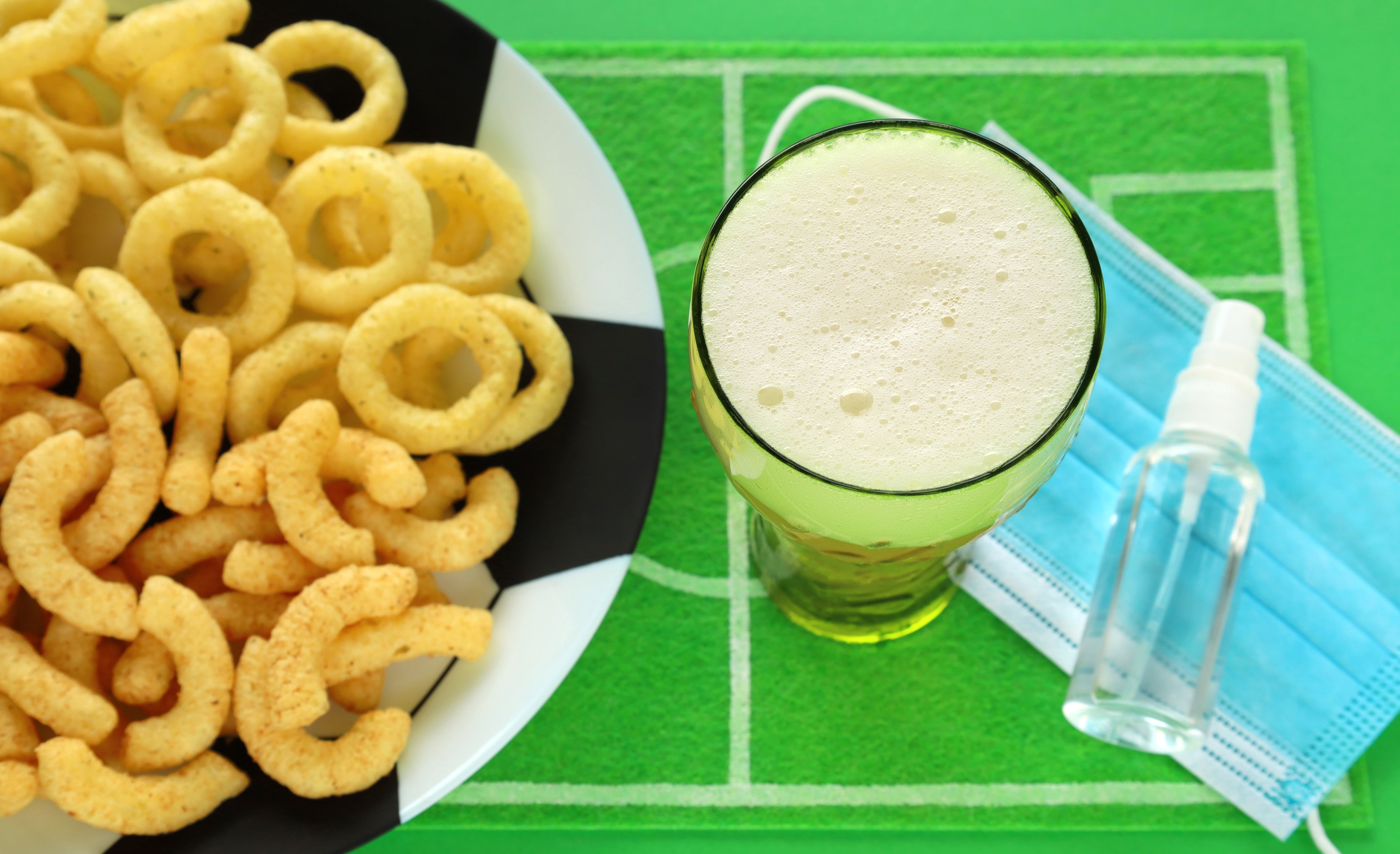 Cerveza, bocadillos para picar y botellita de alcohol en gel sobre cancha de fútbol