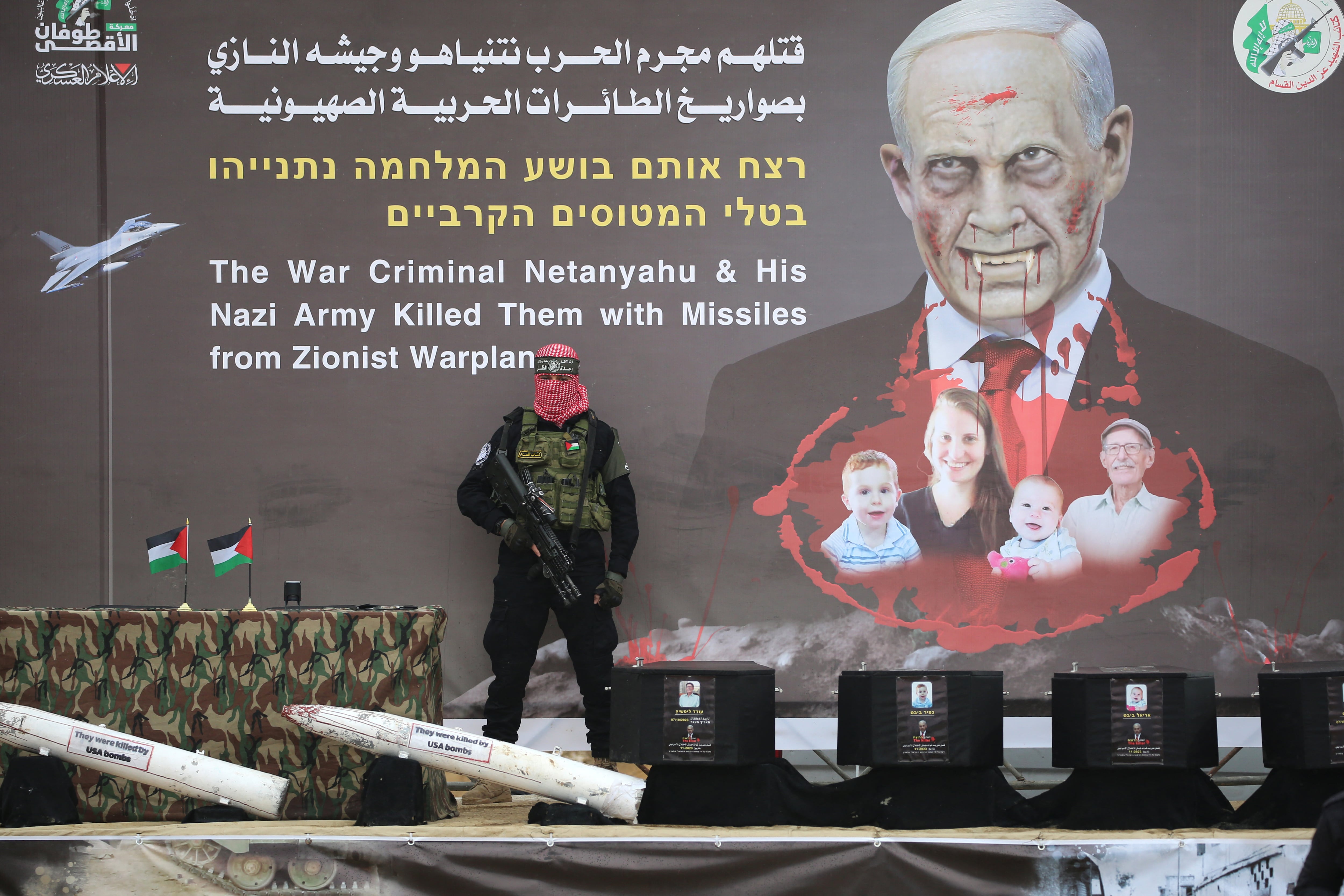 A Palestinian militant group Hamas fighter stands in front of a banner, bearing an altered portrait of Israel's Prime Minister and the Bibas family, on stage ahead of the handing over the bodies of four Israeli hostages in Khan Yunis in the southern Gaza on February 20, 2025. Hamas is due to hand over the bodies of four hostages on February 20, including those of the Bibas family, who have become symbols of the hostage crisis that has gripped Israel since the Gaza war broke out. The transfer of the bodies is the first such hand