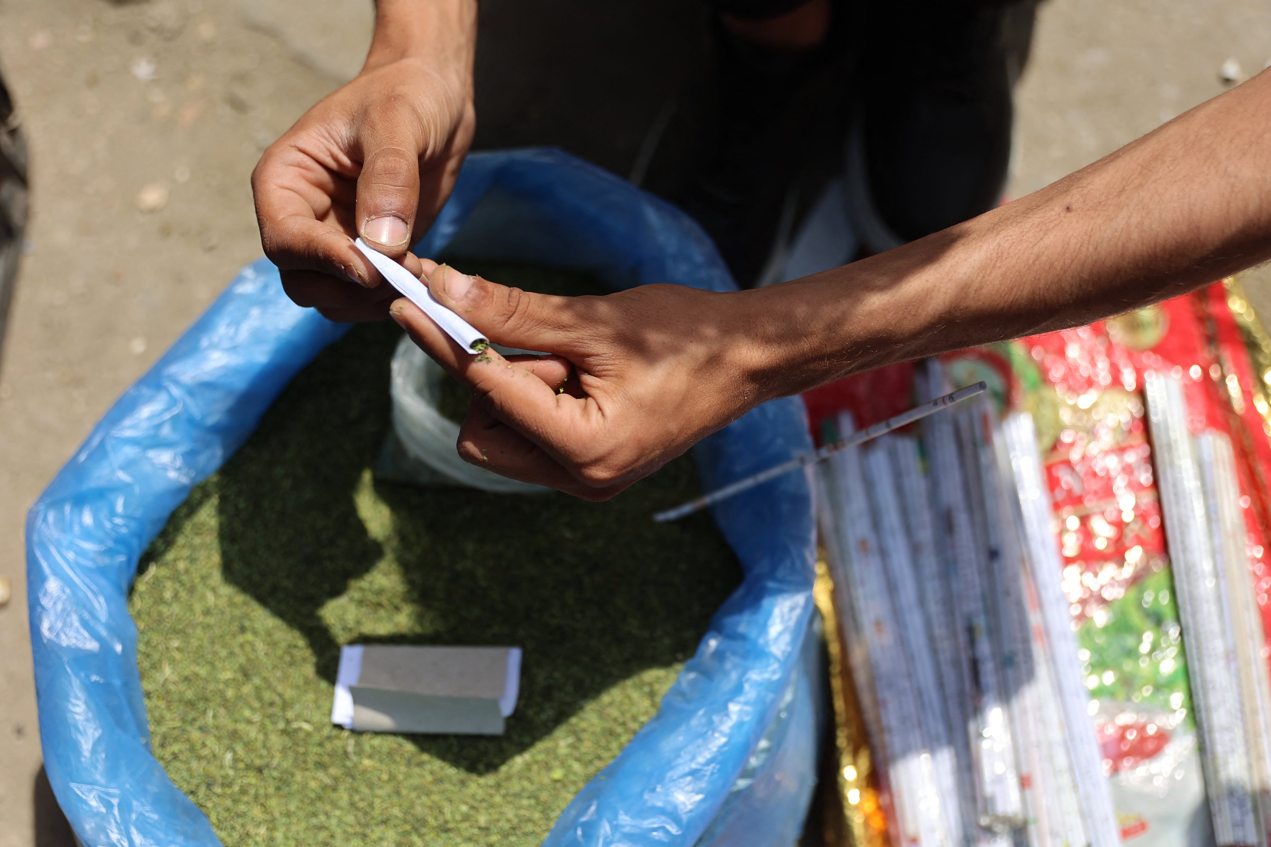 A vendor rolls molokhia leaves, also known as jute mallow, normally used in cooking, into a cigarette at the tobacco market on Omar Al-Mukhtar Street, which traders and residents say is mix with liquid nicotine and processed as smokers turn to improvised alternatives under continuing restrictions that have led to severe shortages in Gaza City and across the enclave on April 19, 2026. In war-ravaged Gaza, where shortages are still acute, some are now smoking home-made roll-ups as a cheaper option as cigarette prices have skyrocketed due to Israel's blockade of many basic goods. Though Gazans normally use molokhia, or jute leaves, for soup, Palestinians now coat the crumbled, dried leaves in liquid nicotine and roll them into cigarettes as a tobacco alternative. (Photo by Omar AL-QATTAA / AFP)