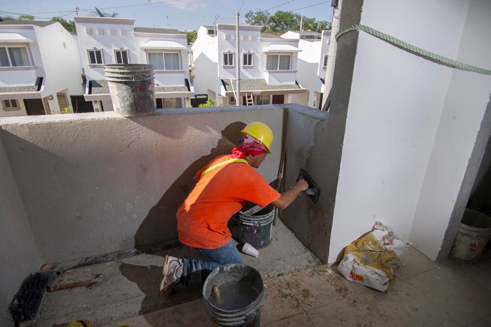 Obrero aplicando cemento en la pared de un condominio en construcción en Costa Rica, con varias viviendas en el fondo. La construcción habitacional sigue en auge en el país.