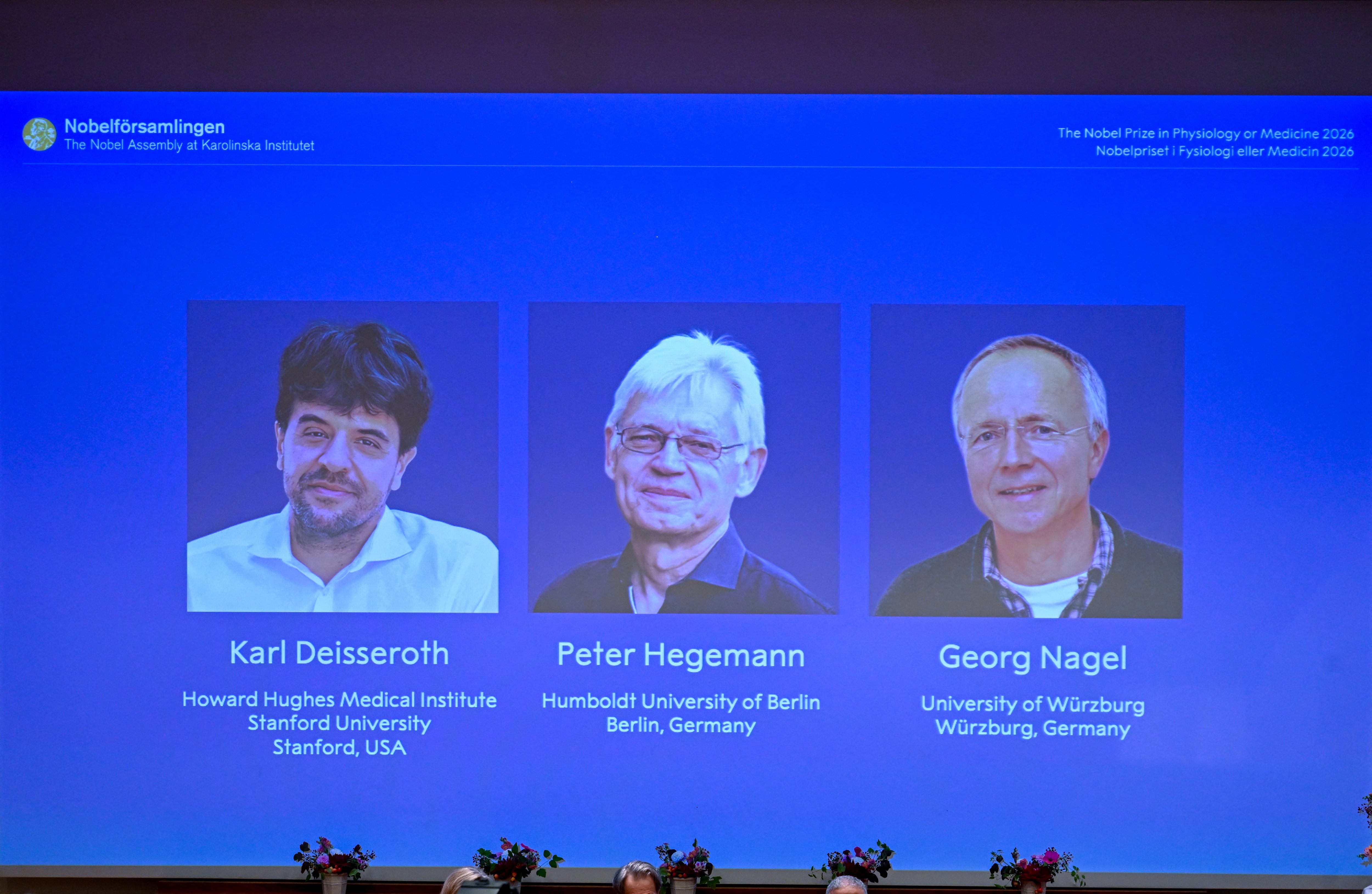 Una pantalla muestra los retratos de (de izq. a der.) el científico estadounidense Karl Deisseroth y los científicos alemanes Peter Hegemann y Georg Nagel durante el anuncio de los ganadores del Premio Nobel de Fisiología o Medicina 2026 en el Instituto Karolinska en Estocolmo, Suecia, el 5 de octubre de 2026. El científico estadounidense Karl Deisseroth y los científicos alemanes Peter Hegemann y Georg Nagel comparten el Premio Nobel de Fisiología o Medicina 2026 por sus descubrimientos sobre los canales iónicos activados por luz y la optogenética. (Foto de Jonathan Nackstrand / AFP)