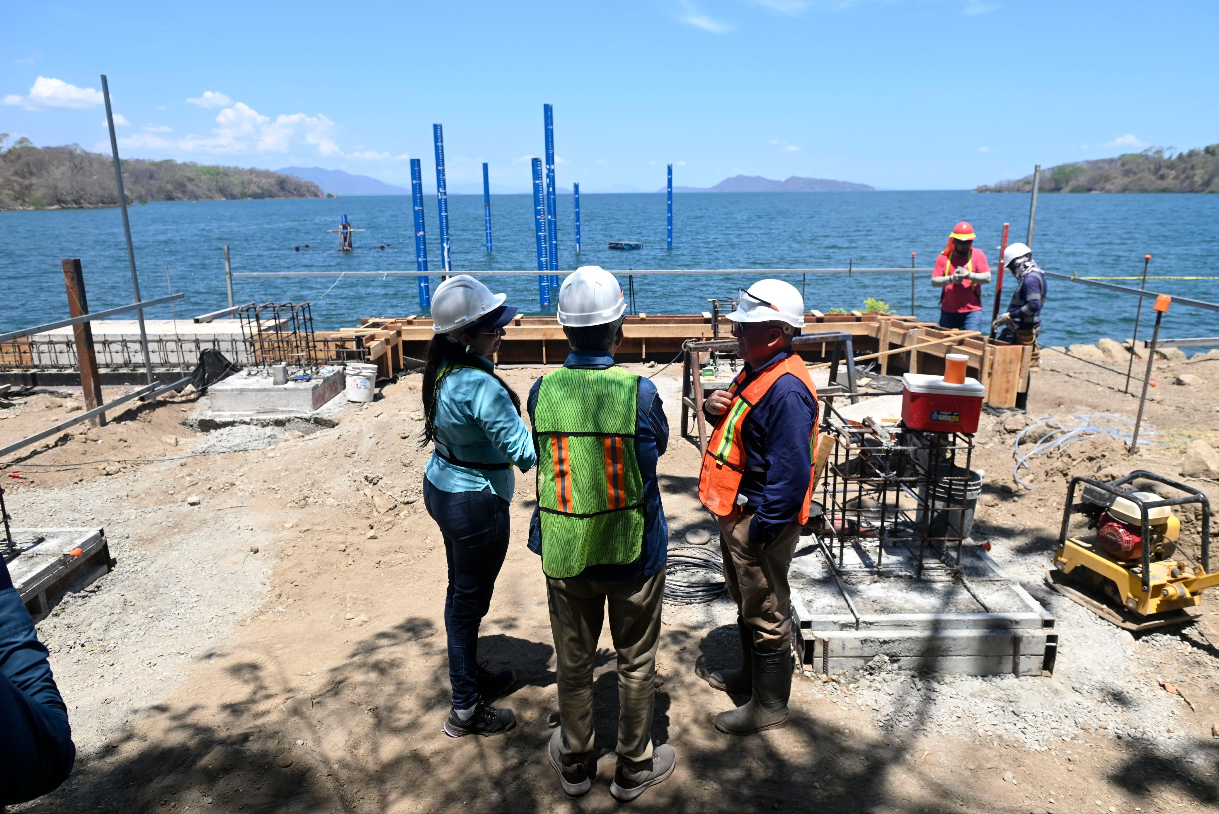 Funcionarios y trabajadores revisan obra del embarcadero turístico en isla San Lucas, Puntarenas, con pilotes instalados en el mar y avance en infraestructura.