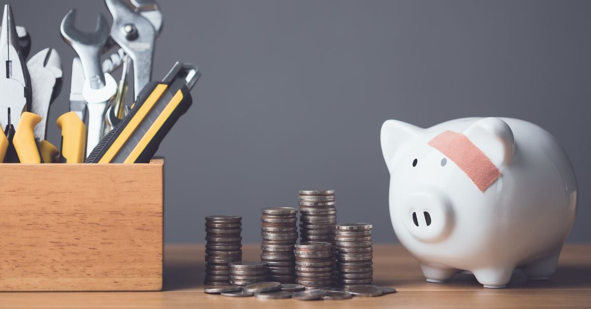 En la imagen, un chanchito de ahorro con una caja de herramientas, monedas, y una curita