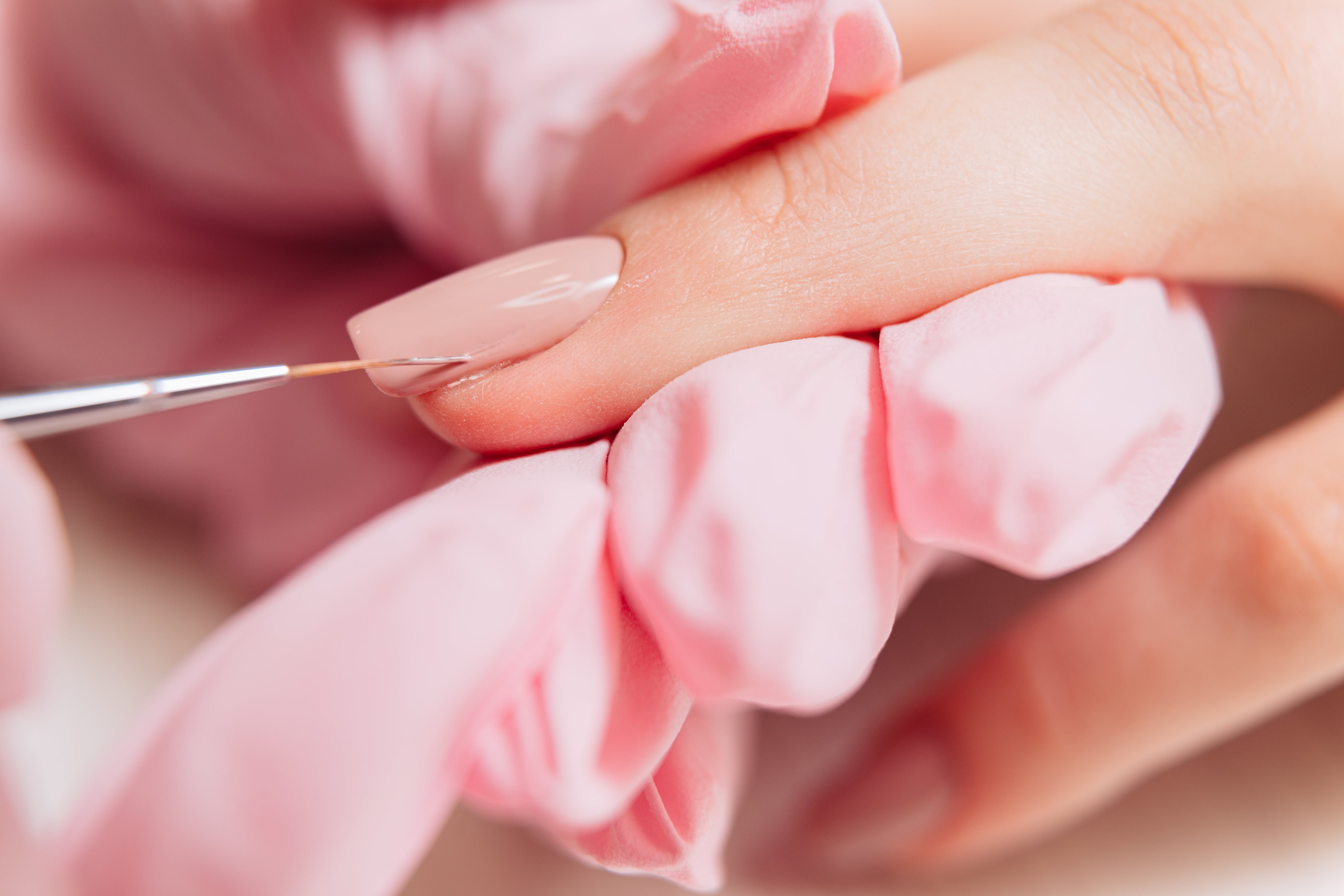 Una mano recibiendo manicure, otra mano la pinta.