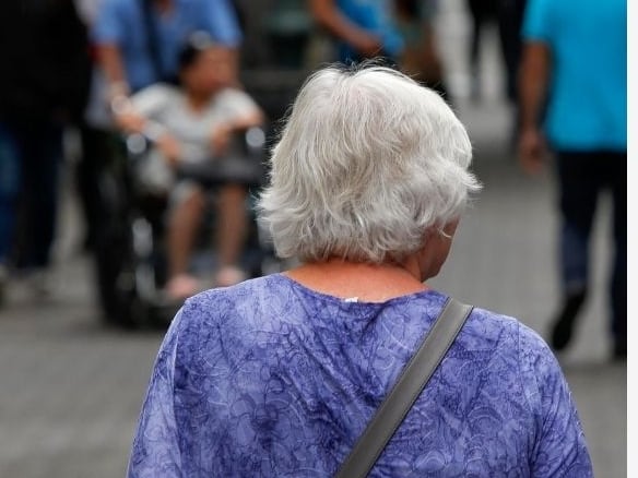 Mujer adulta mayor de espaldas caminando por la avenida central de San José.