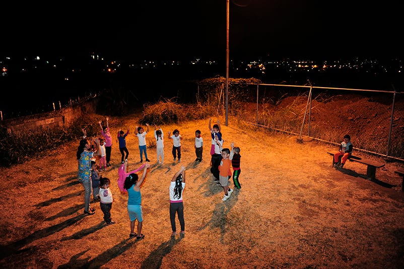 Niños participando en una actividad grupal nocturna al aire libre en un barrio con iluminación limitada. Reflejo de la importancia de la comunidad en zonas vulnerables.